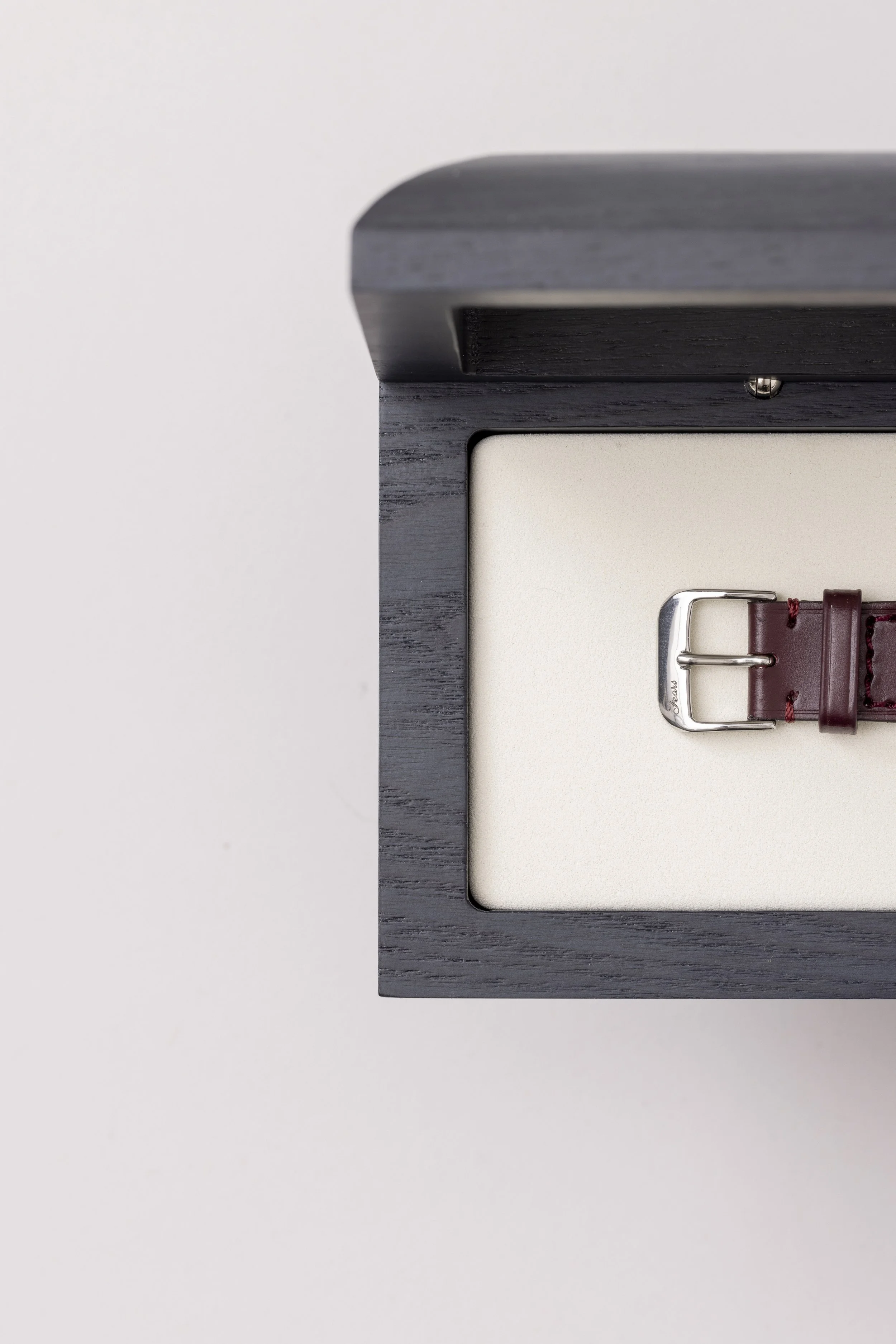Close-up of a black wooden frame with a beige slide and a red watch strap with a silver buckle.