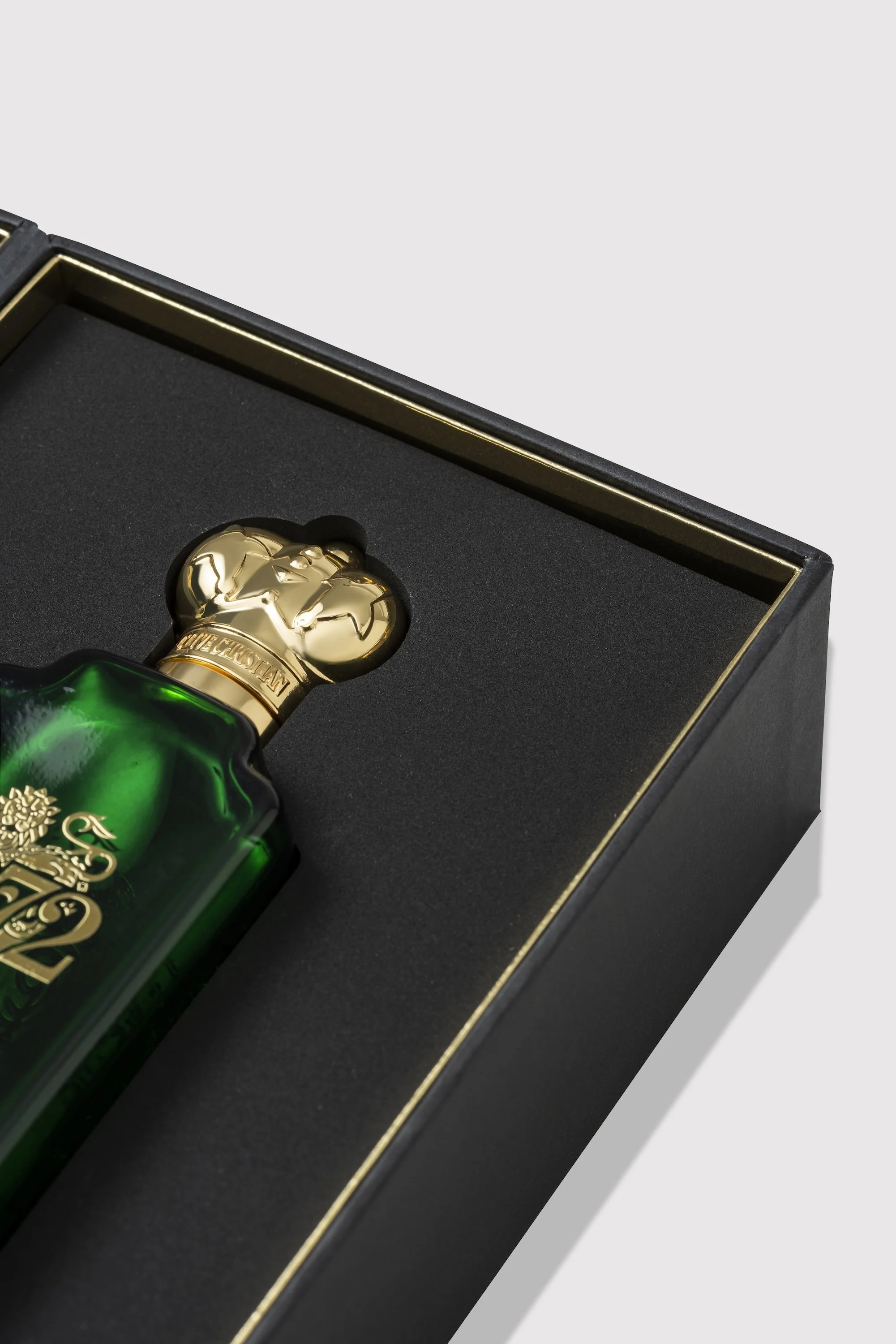 A close-up of a green glass bottle with a gold skull-shaped cap, inside a black box with gold trim.
