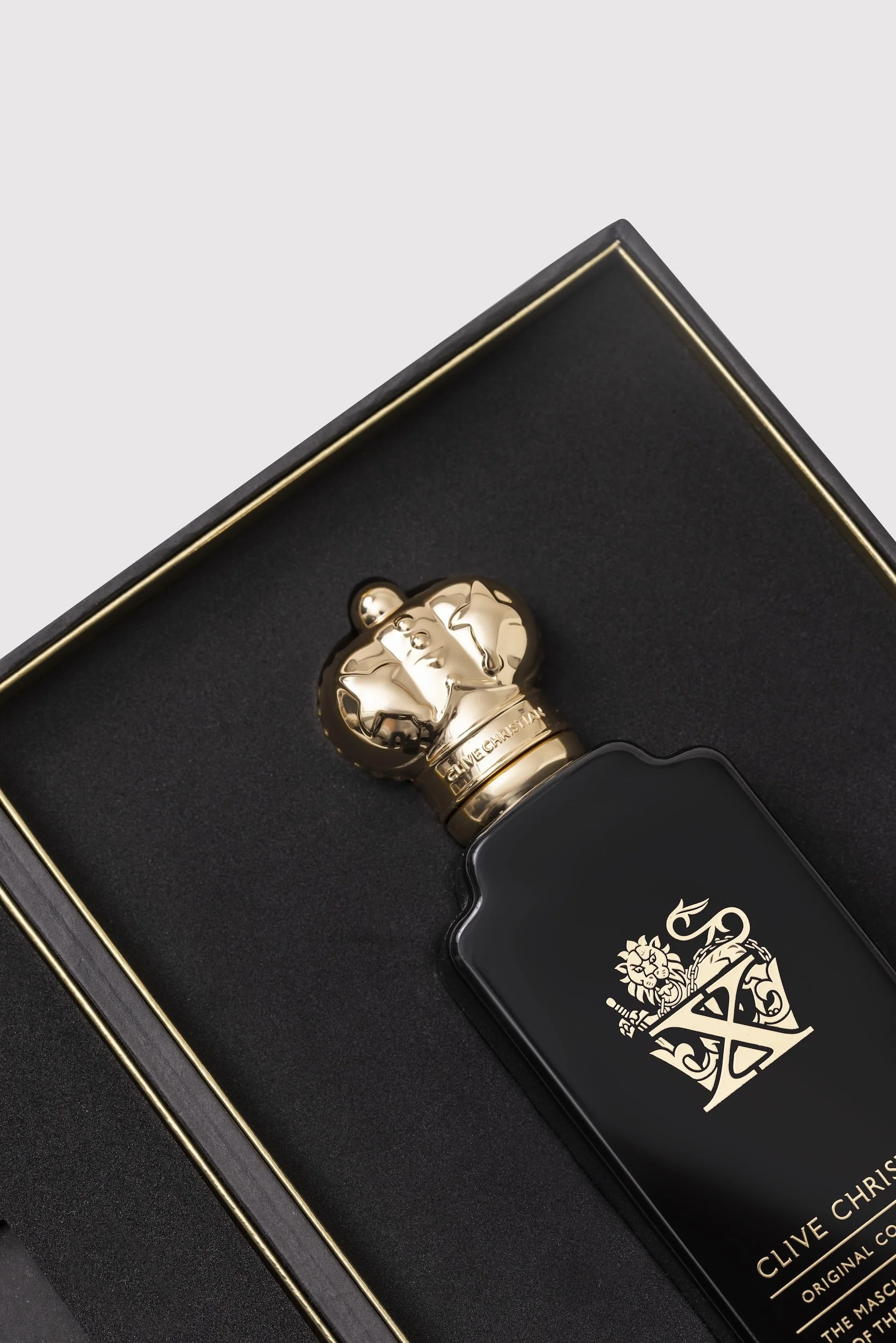 Close-up of a luxury perfume bottle with a gold lion head cap, in a black and gold boxed presentation. The box has the Gucci logo and crest printed on it.