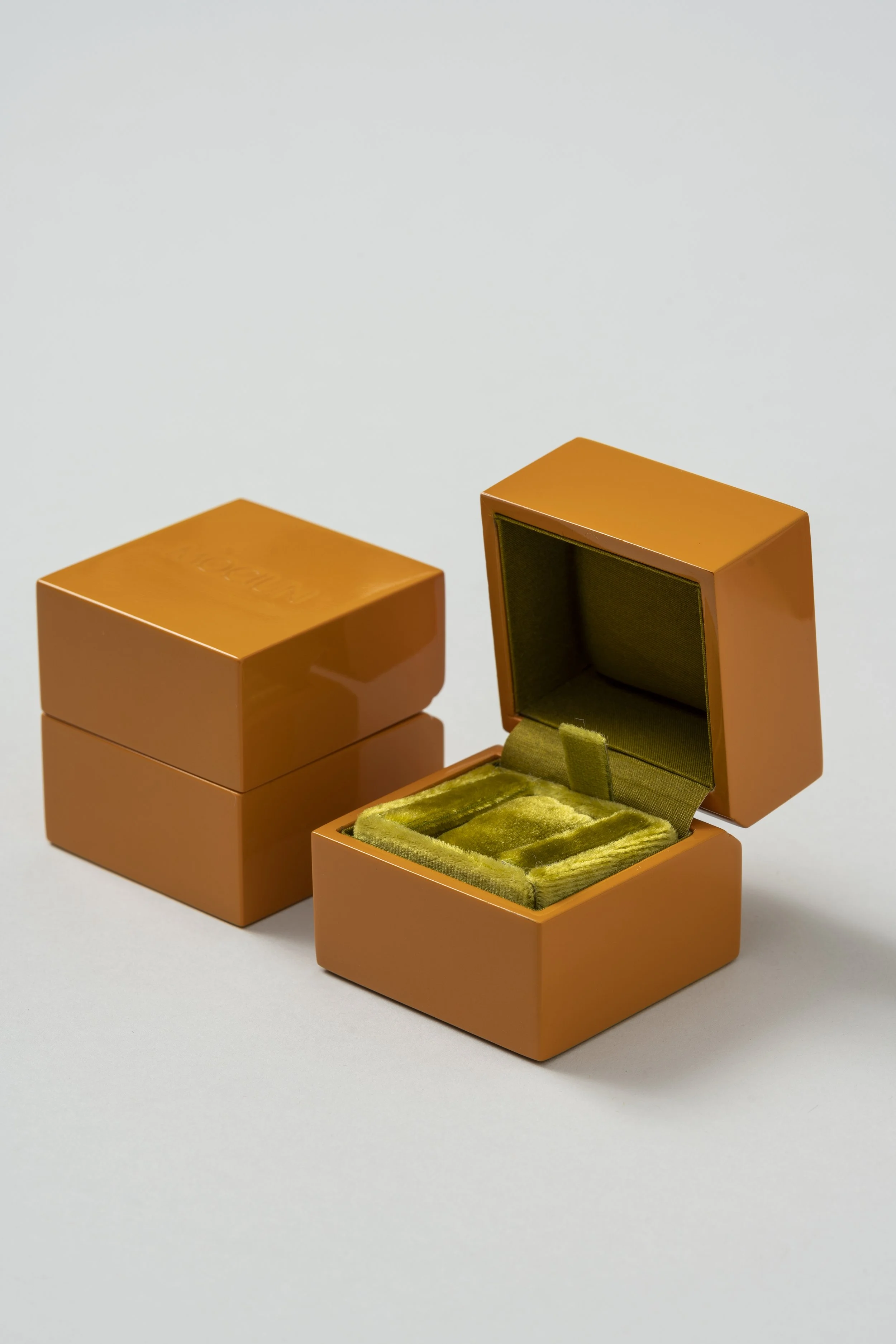 Open orange jewelry box with green velvet interior, next to two closed matching boxes, on a white background.