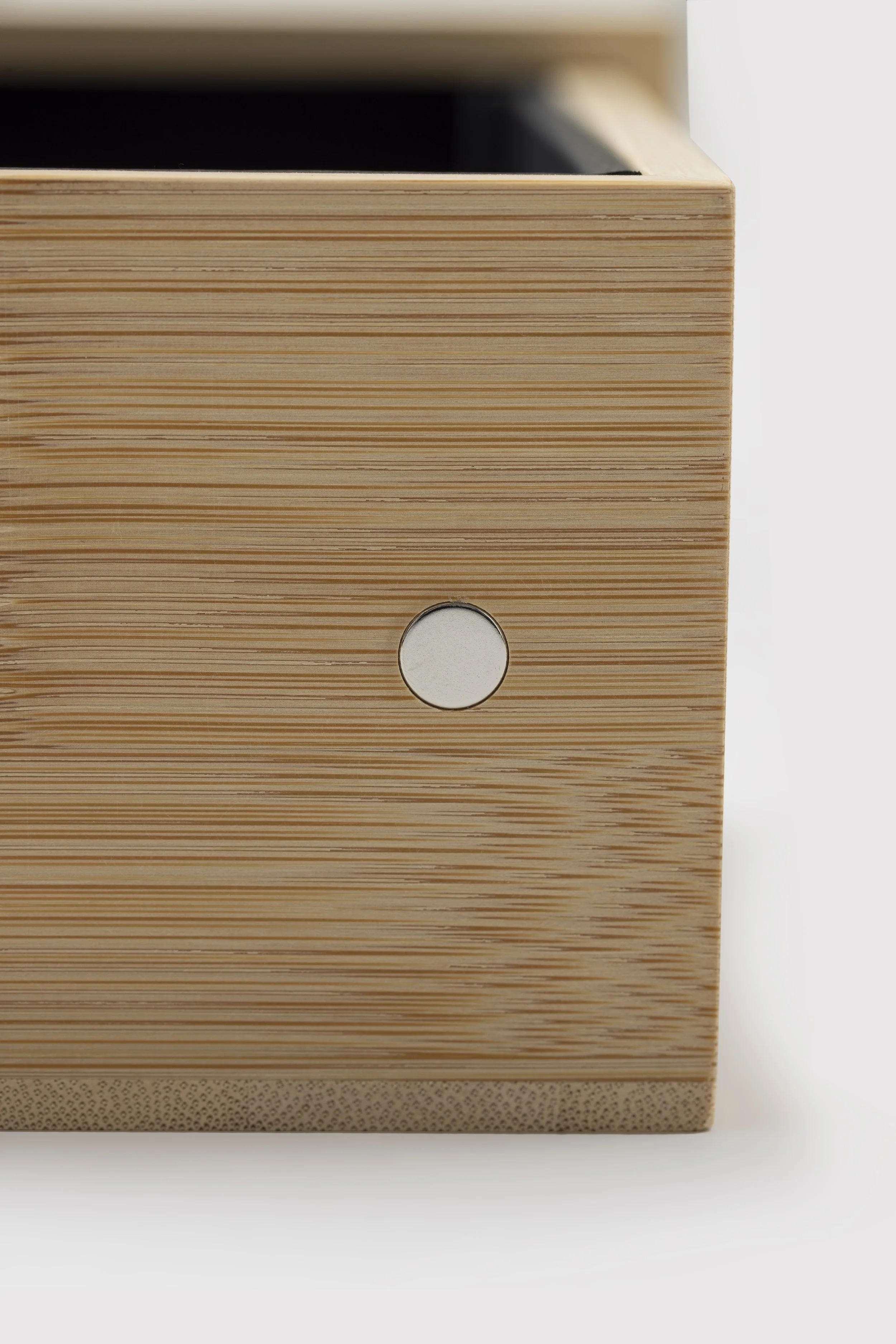Close-up of a wooden speaker with a circular hole on the front panel, sitting on a white surface.