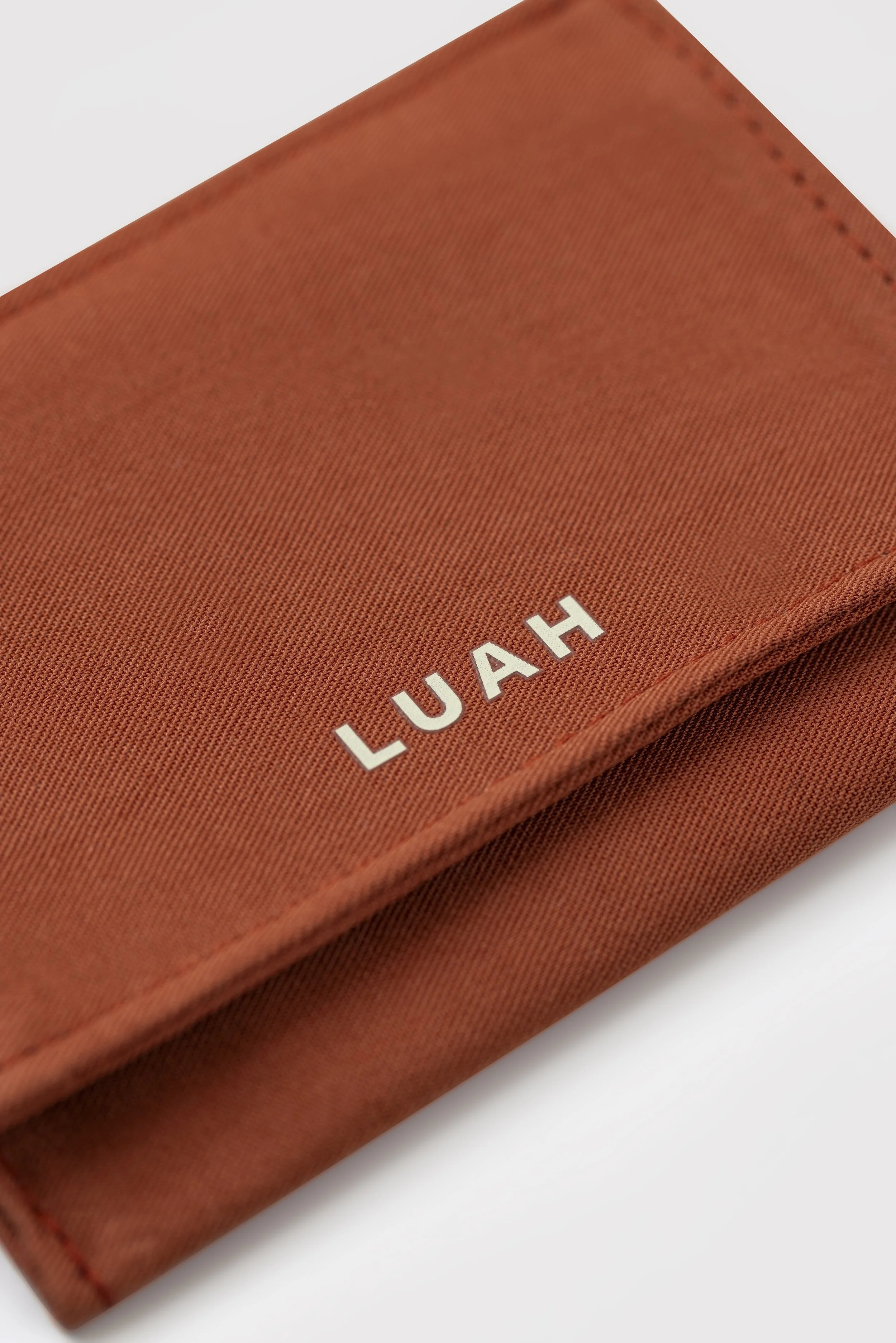 Close-up of a red fabric wallet with white text that reads 'LUAH' on the corner.