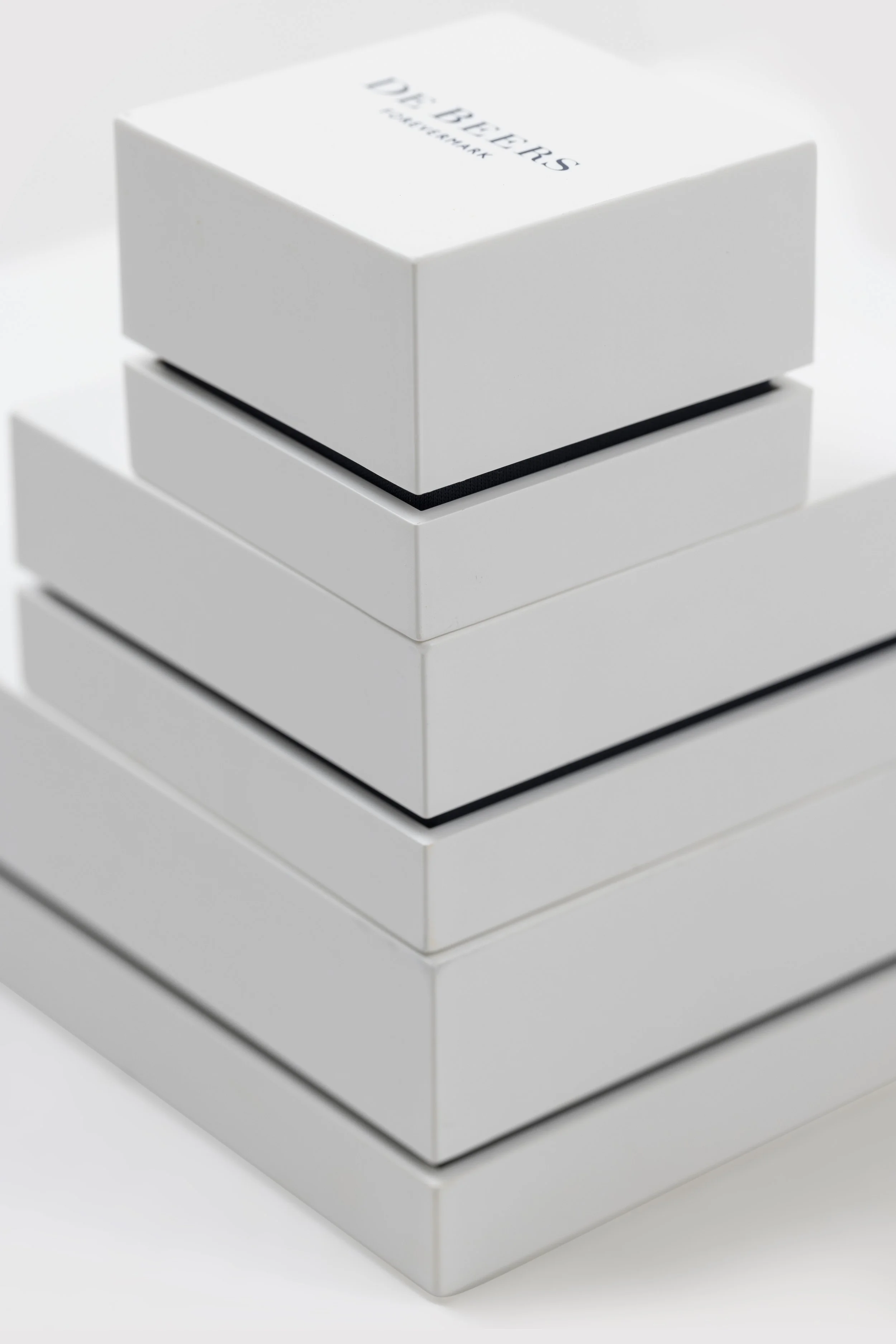 Stack of white jewelry boxes with black interior lining, arranged in a vertical column on a white surface.