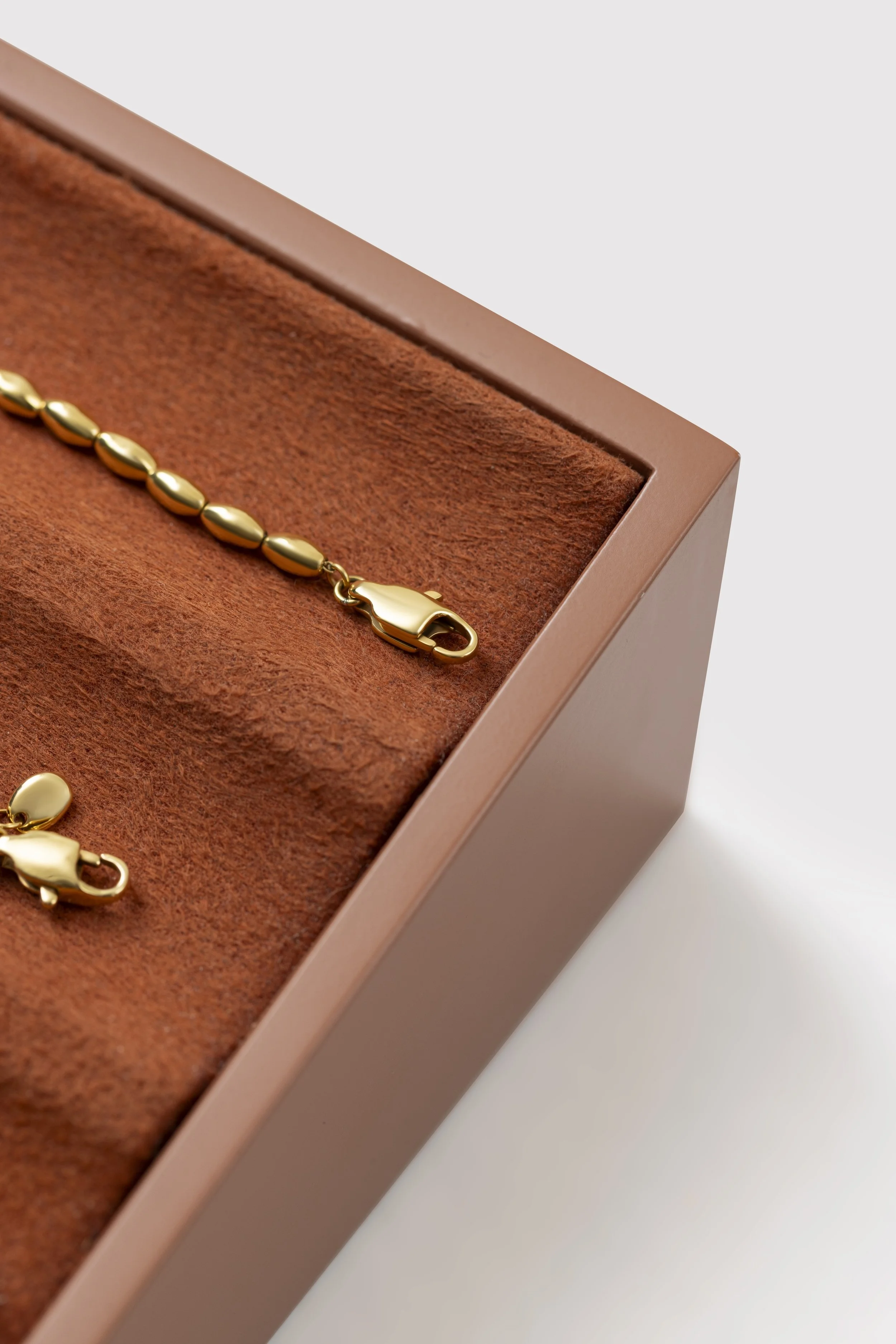 Close-up image of a gold bracelet in a jewelry box with a brown velvet interior, part of a pink-colored jewelry box edge visible.