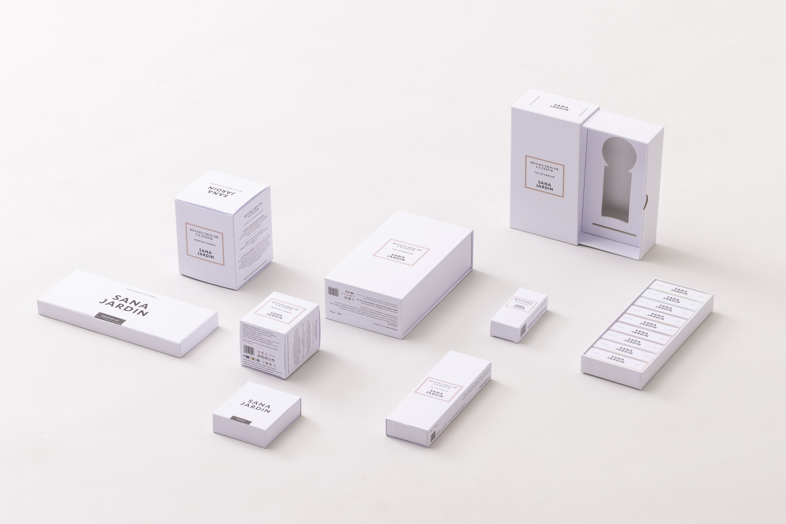Multiple white perfume boxes and bottles arranged on a white surface, with the brand name 'SANA JARDIN' and product name 'REVOLUTION DE LA FLEUR' printed on the packaging.