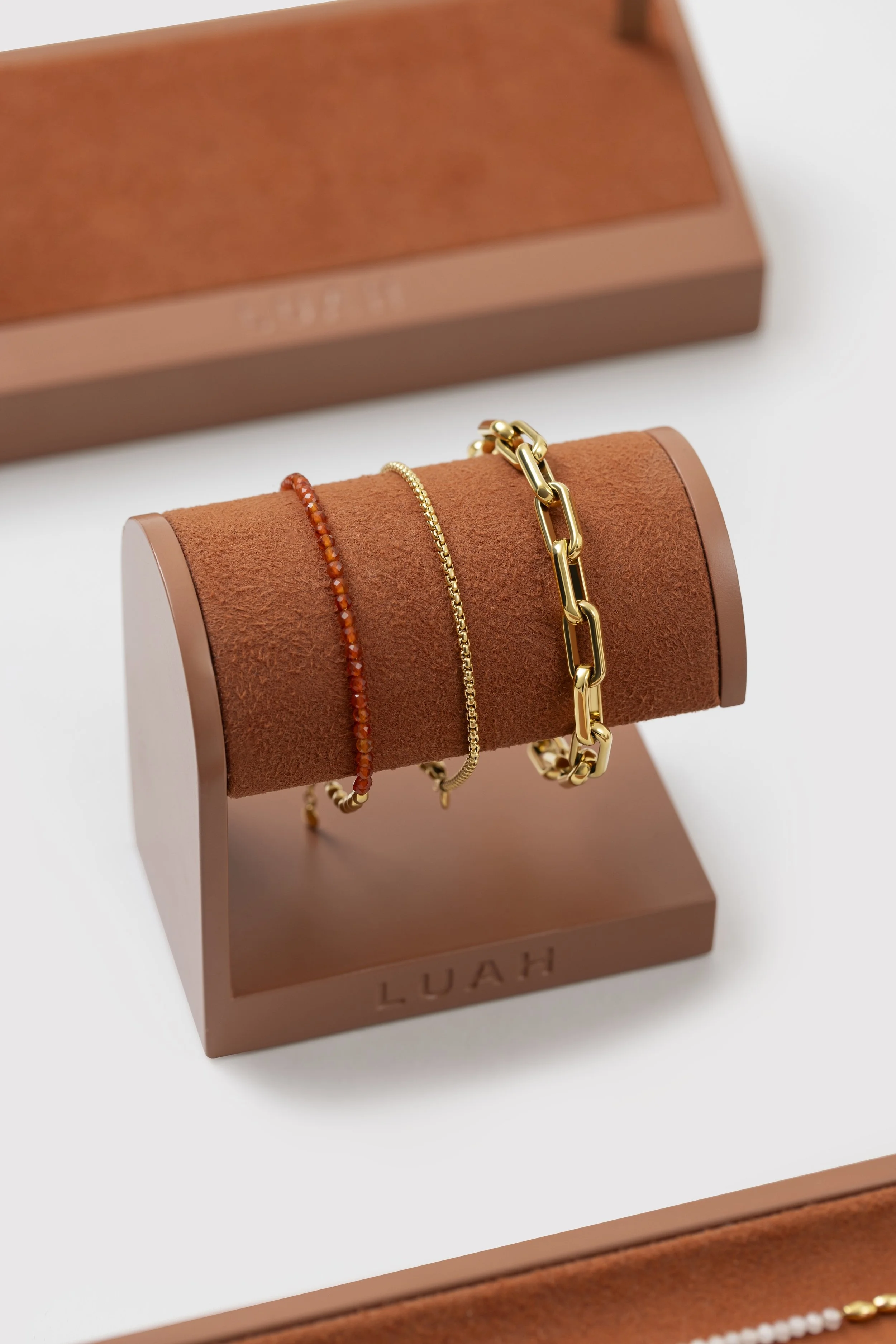 Gold jewelry bracelets on a brown jewelry display stands with a box in the background labeled 'LUAH'.