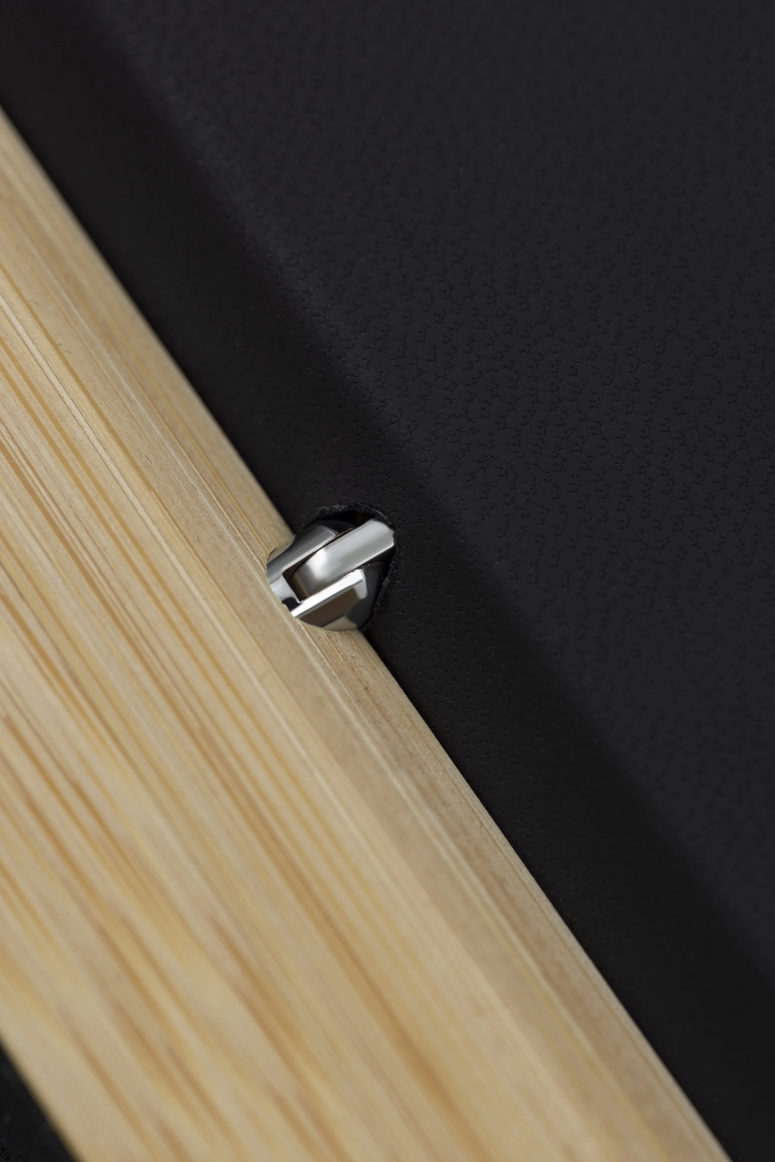 Close-up of a hinge connecting a black surface to a wooden surface.