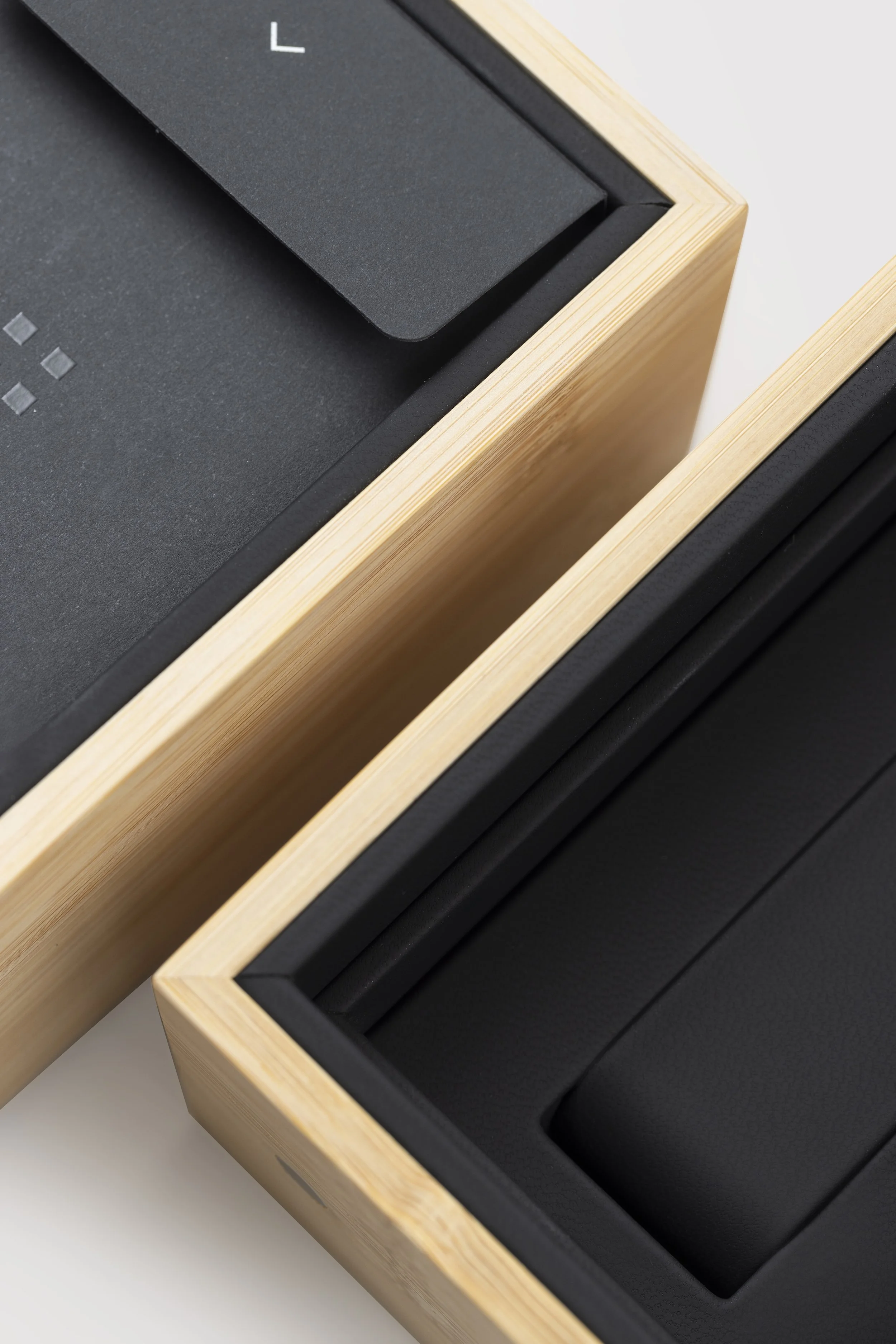 Close-up view of a wooden box with a black interior, possibly for storing items, with a black foam insert inside.