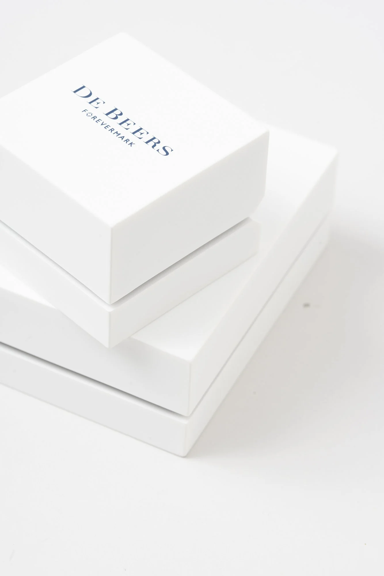 Close-up photo of a white box labeled 'DE BEERS FOREVERMARK' placed on top of a similar-looking white box, against a plain white background.