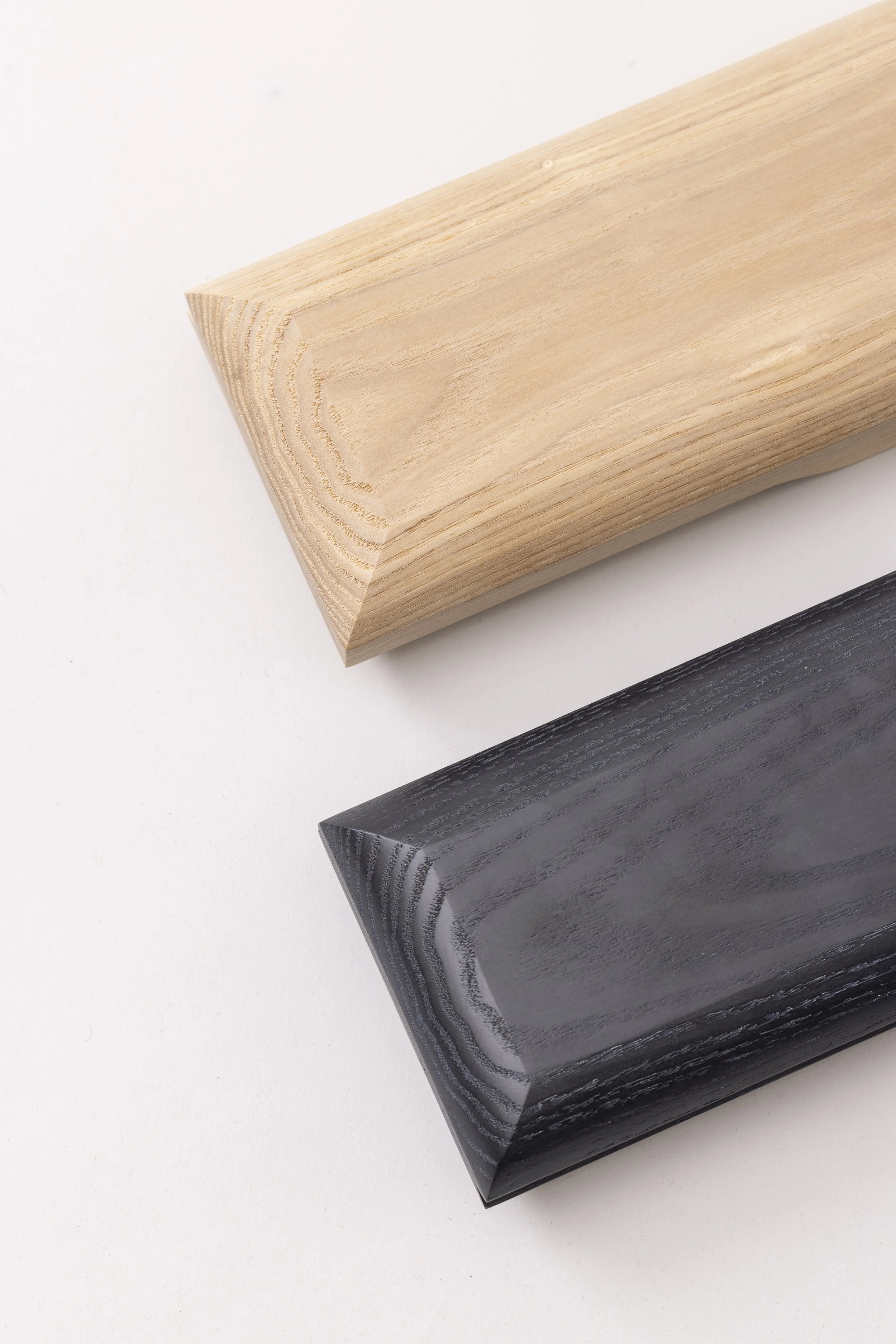 Close-up of three rectangular blocks of wood in different colors: natural light wood, whitewashed wood, and black stained wood, arranged diagonally on a white background.