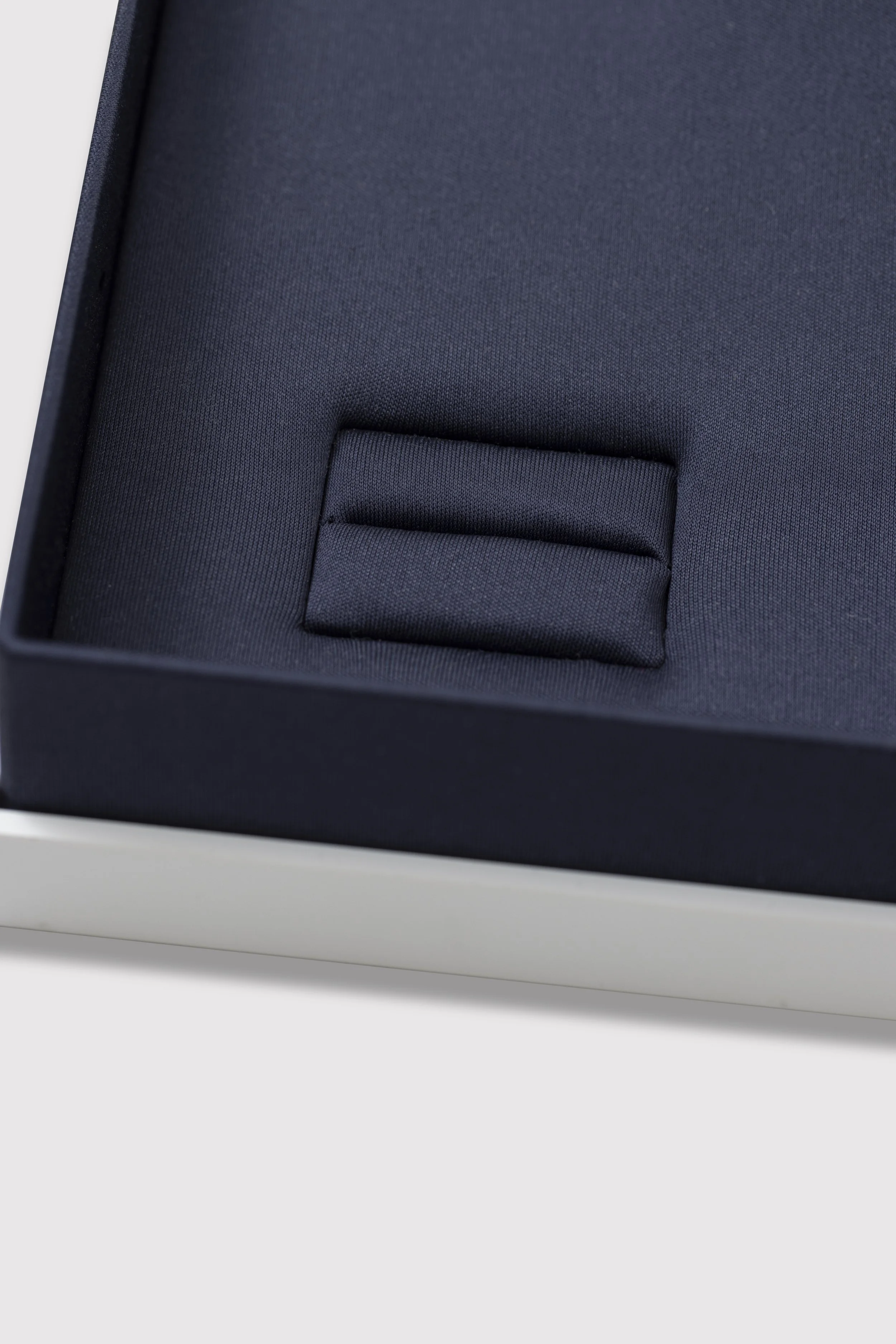 Close-up of a black jewelry box with a padded interior, inside which is a small flat object, possibly a ring or similar jewelry, held in a slot.