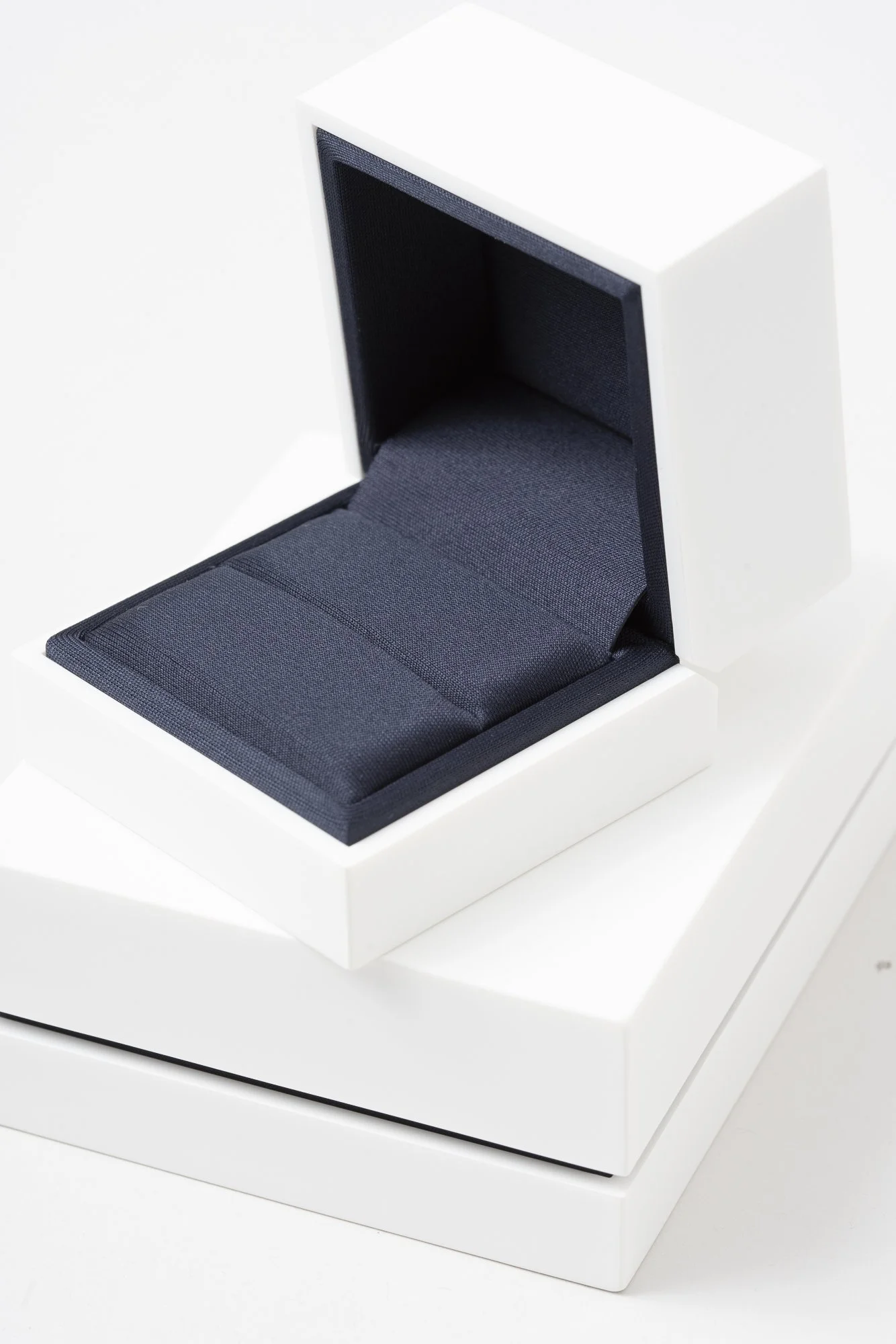 A white box with a black cushioned interior, open to reveal a padded section, possibly a jewelry or watch display case.