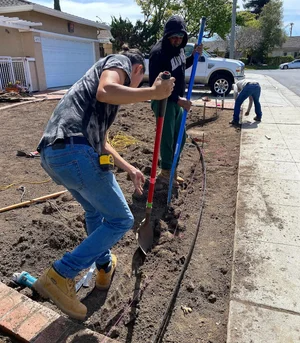 Crew member digging a trench for a new planting strip beside a sidewalk