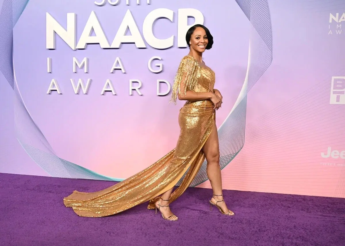 A woman in a shiny gold gown with a high slit posing on a purple carpet at the NAACP Image Awards.