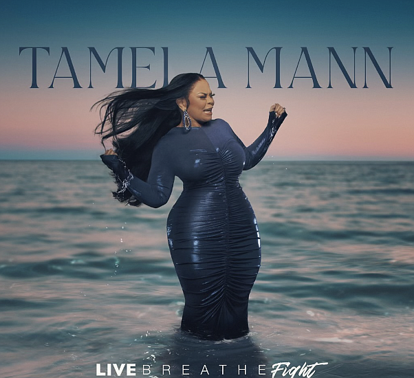 Tameka Mann standing in the ocean during sunset, wearing a dark, shiny, form-fitting dress with long sleeves.