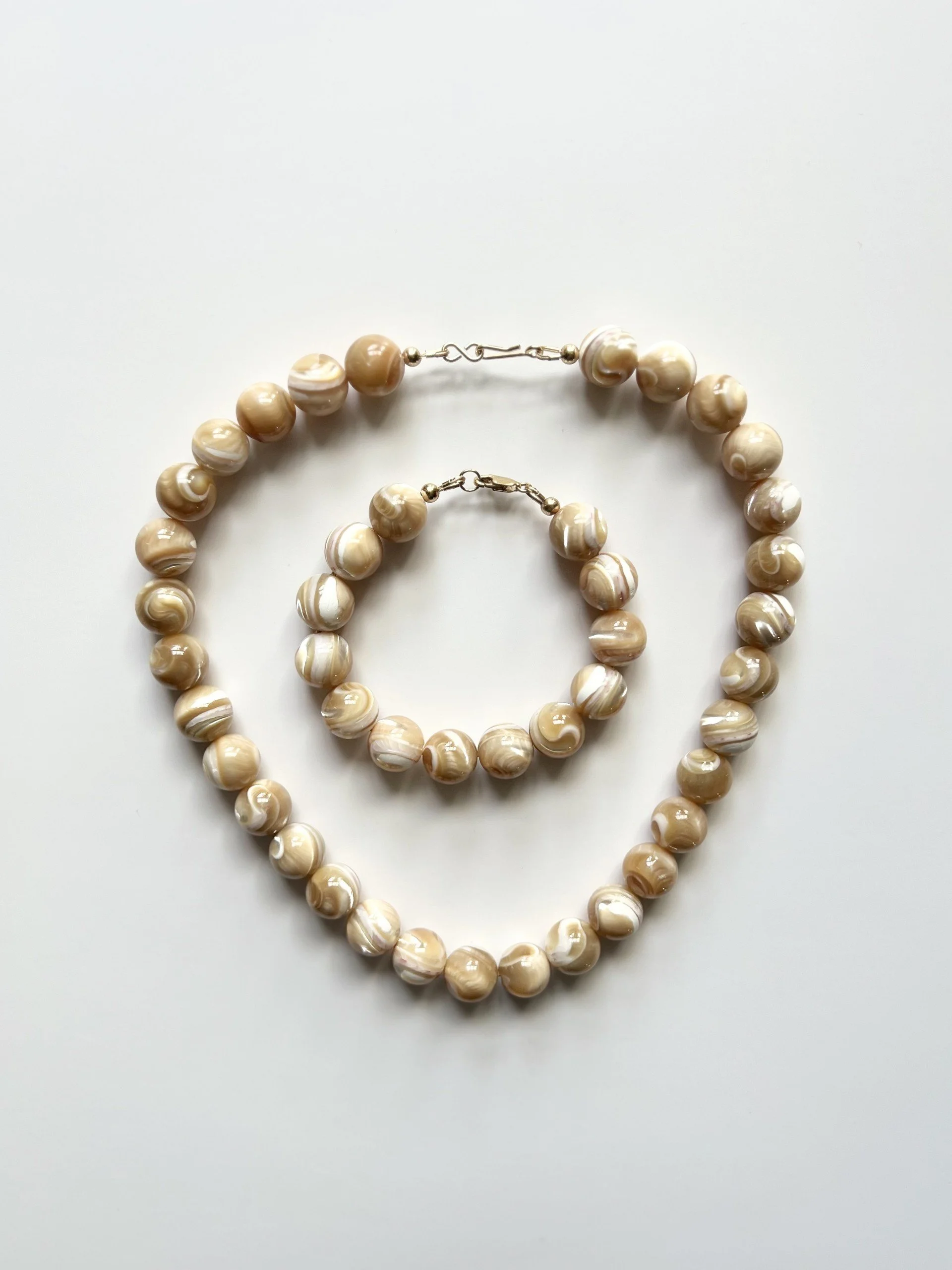 Beaded necklace with beige and white swirl effect beads called caramel mother of pearl necklace and bracelet on a white background with gold filled clasps.