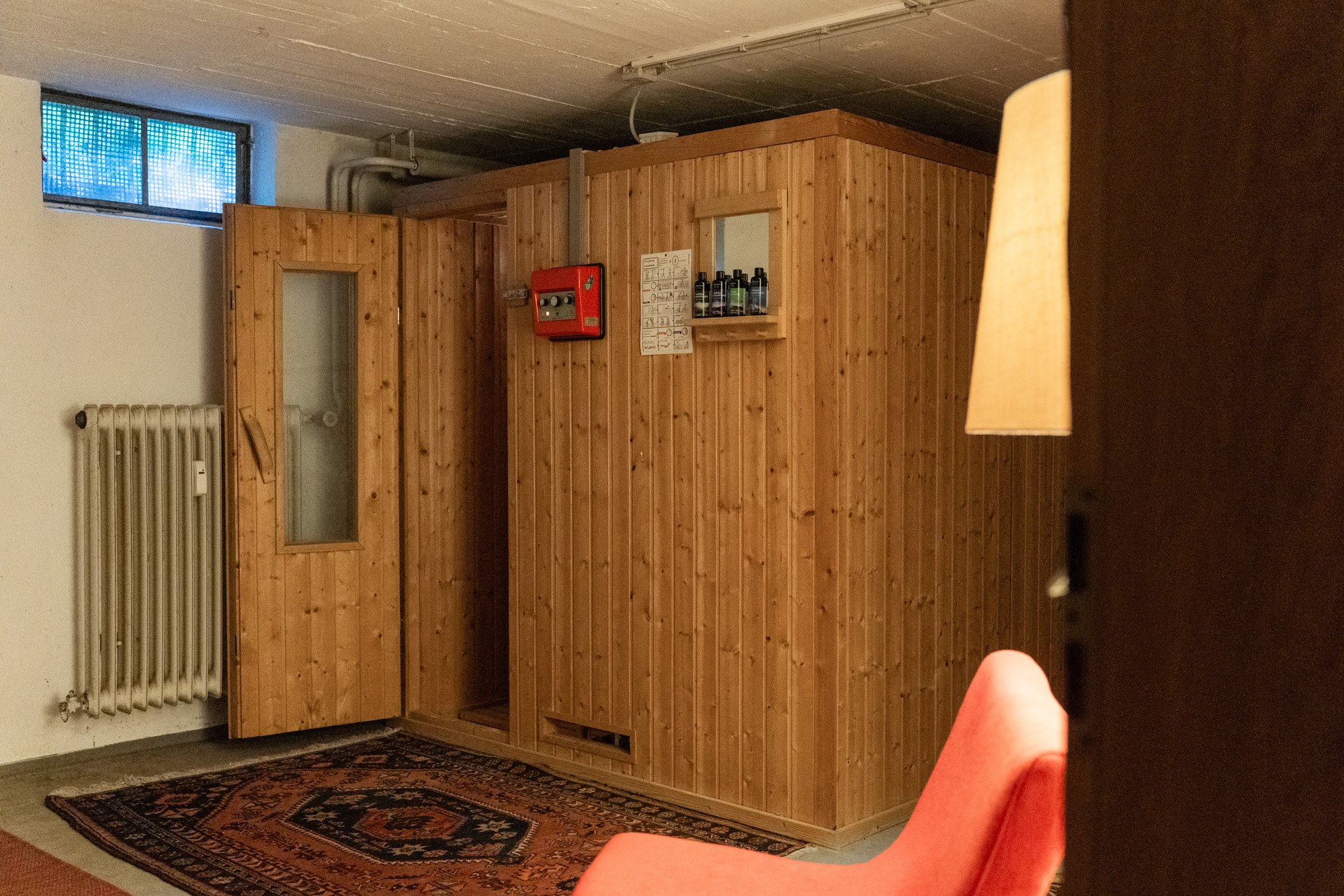 Foto eines kleinen beheizten Saunaraums mit Holzverkleidung, klarem Fenster, Teppichboden und Sitzgelegenheit.