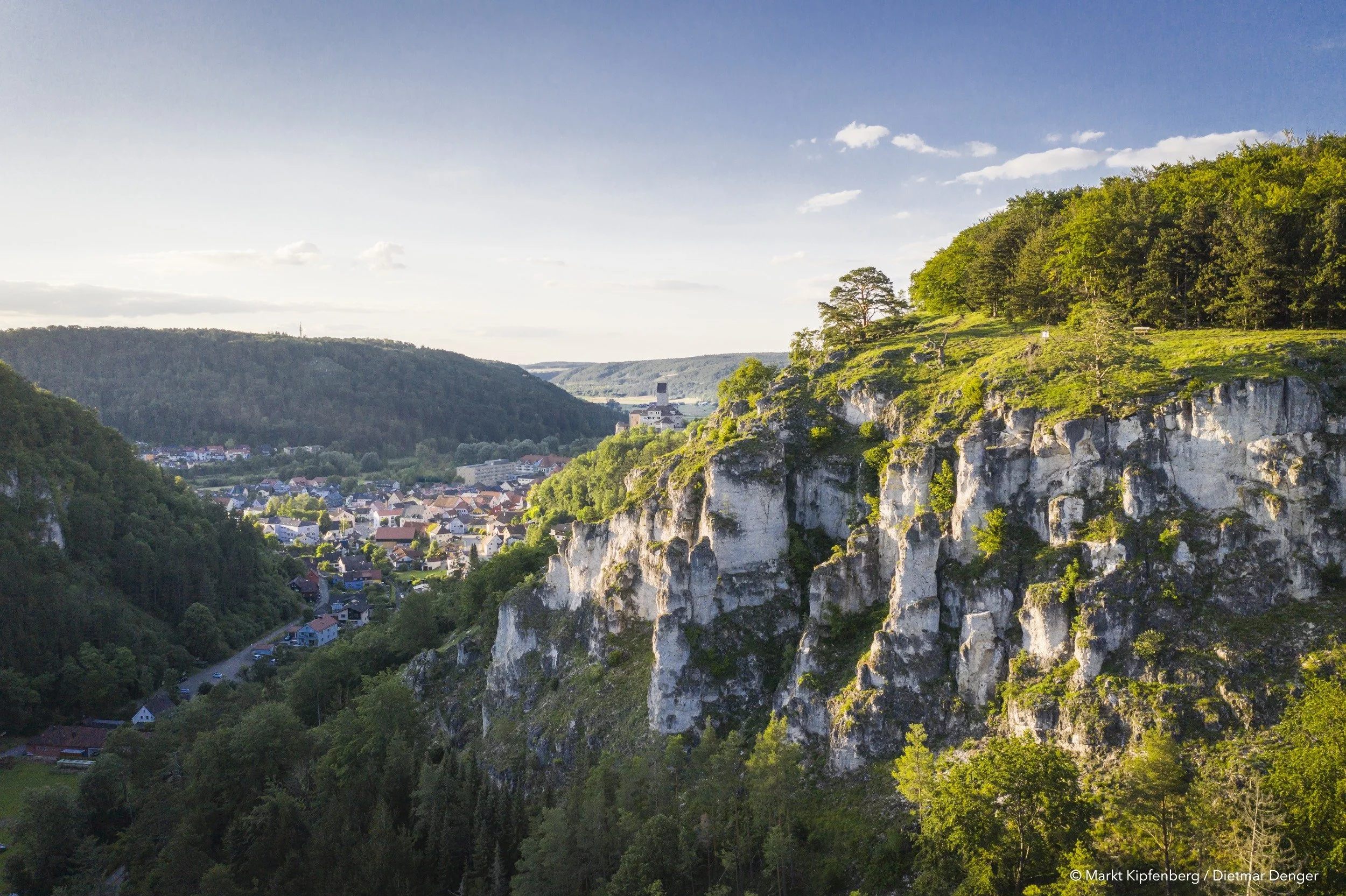 Landschaft mit einem Fluss, grünen Hügeln, Bäumen und einer Kleinstadt im Tal bei Tageslicht.