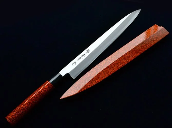 A Japanese kitchen knife and sharpening stone on a black background.
