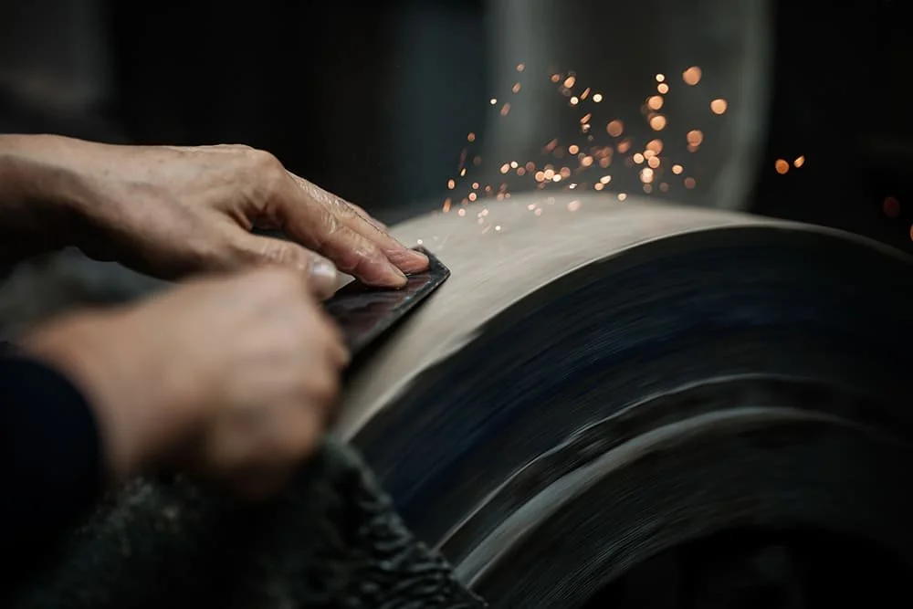 Close-up of a person's hands grinding a metal piece on an abrasive wheel with sparks flying.