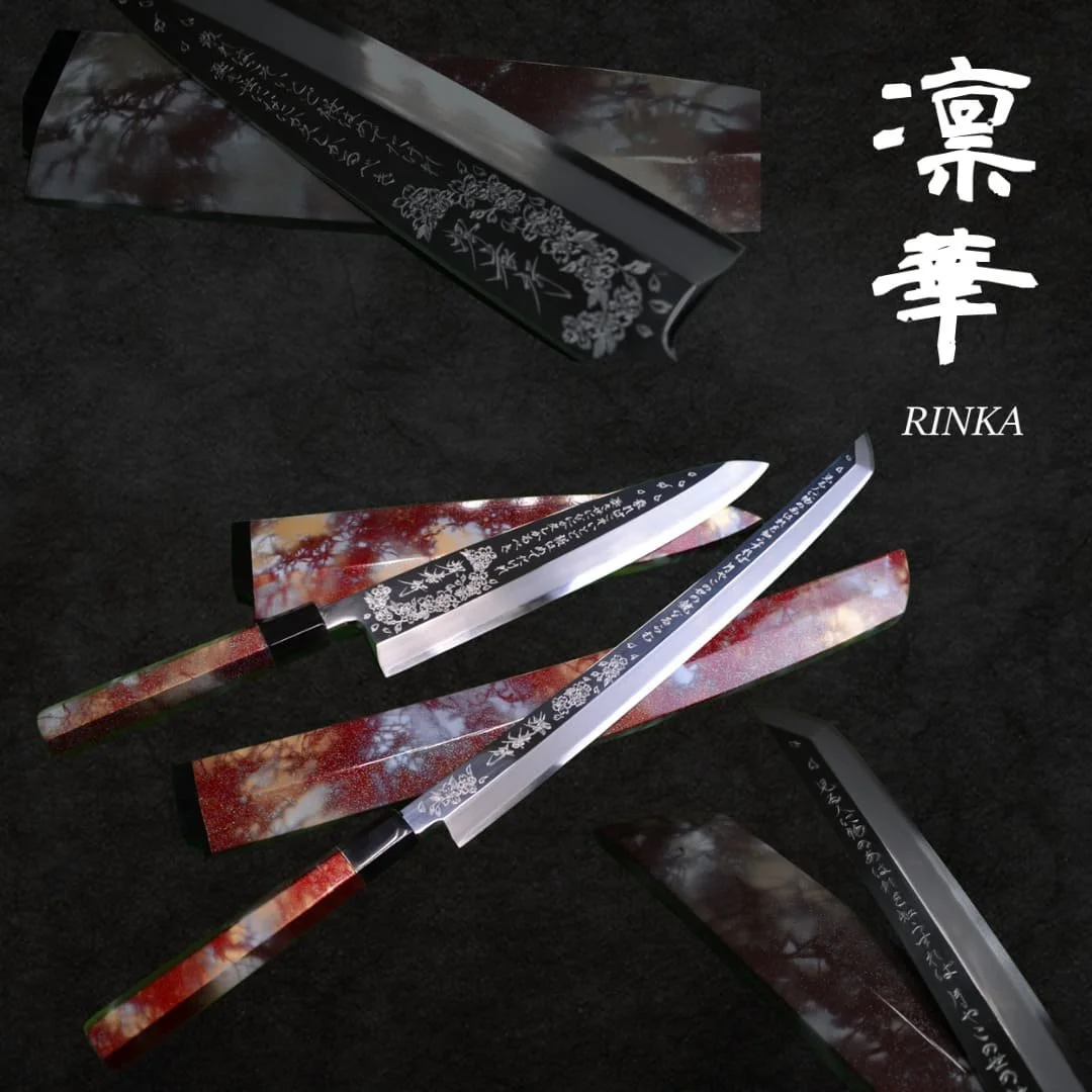 A decorative kitchen knife with a black handle and silver blade, with Japanese characters and floral designs engraved on it, placed on a black surface along with a box and a sheath that have matching patterns.