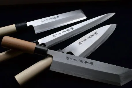 Four Japanese kitchen knives with wooden and plastic handles on a black background.