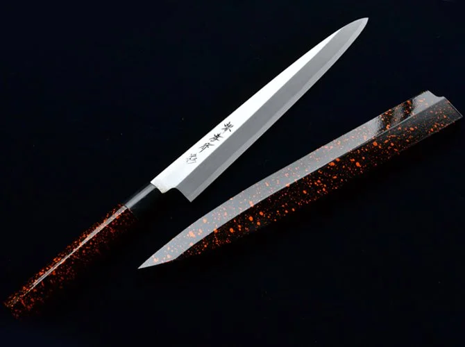 A Japanese kitchen knife with a white blade and black handle with red glitter, placed next to a matching blade cover with red glitter on a black background.