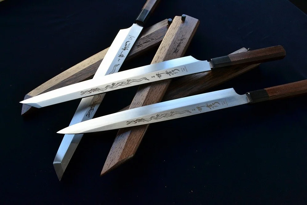 Three Japanese-style kitchen knives with wooden handles on top of Japanese sharpening stones on a black surface.