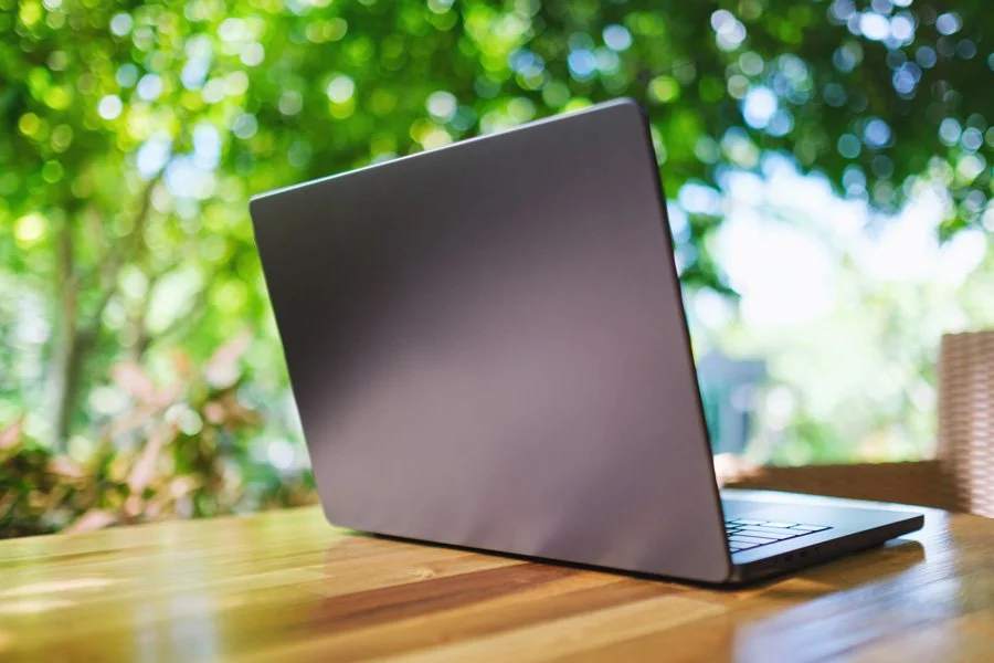 A silver laptop on a wooden table with a blurred green outdoor background.