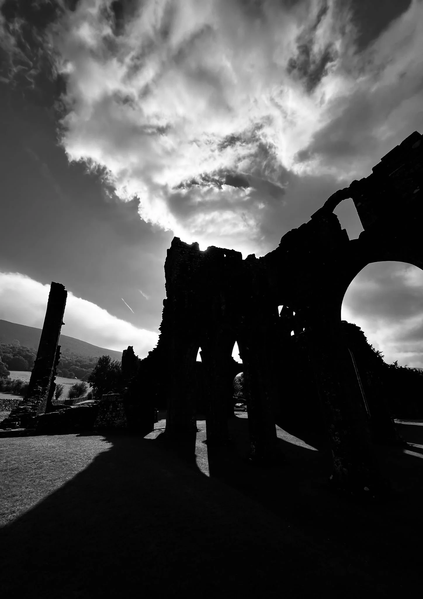 Silhouette of ancient stone ruins against a cloudy sky with sunlight peeking through.