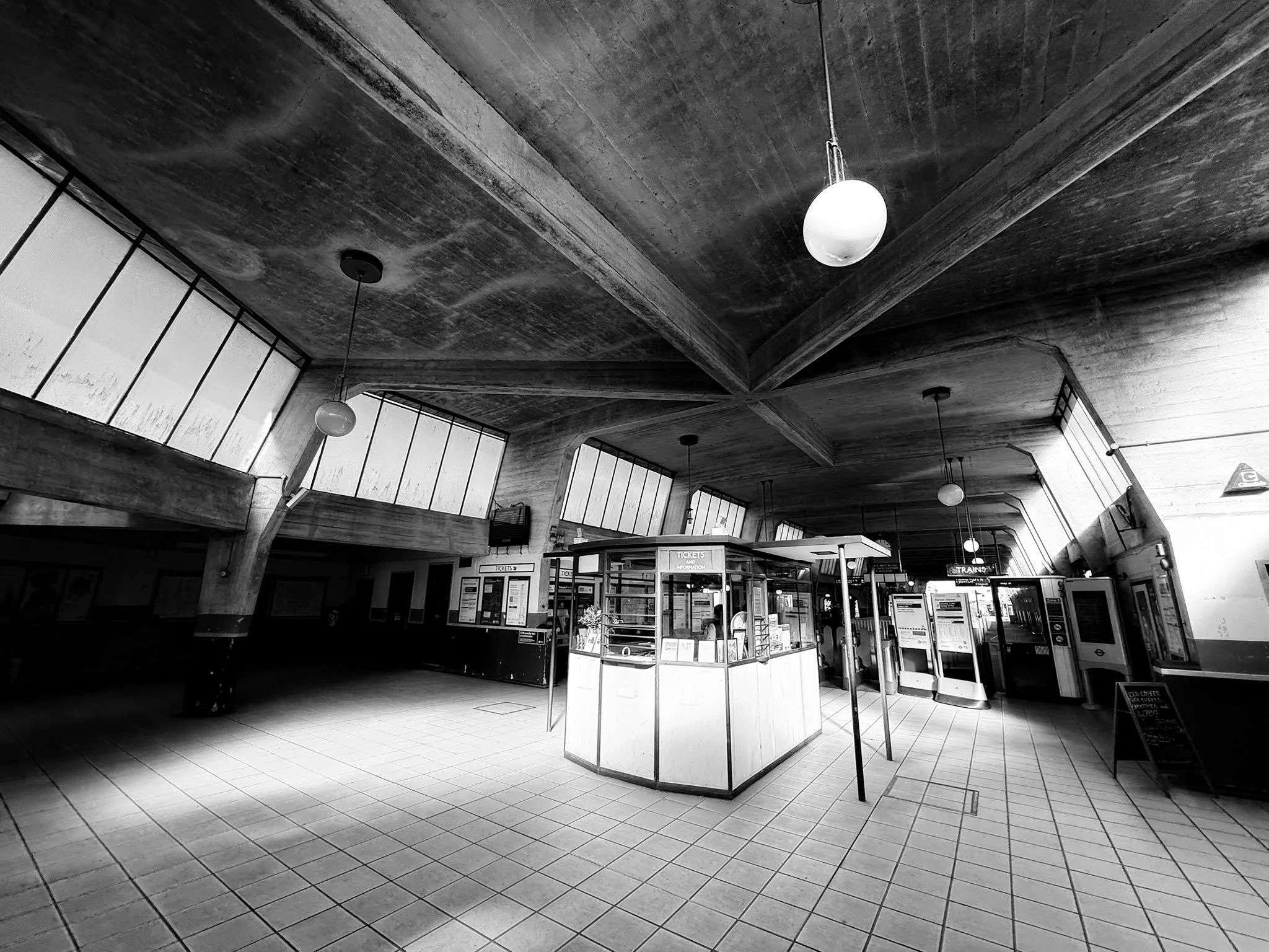 Interior of a train station or transportation hub with ticket counters, metal detectors, and large windows on the ceiling.