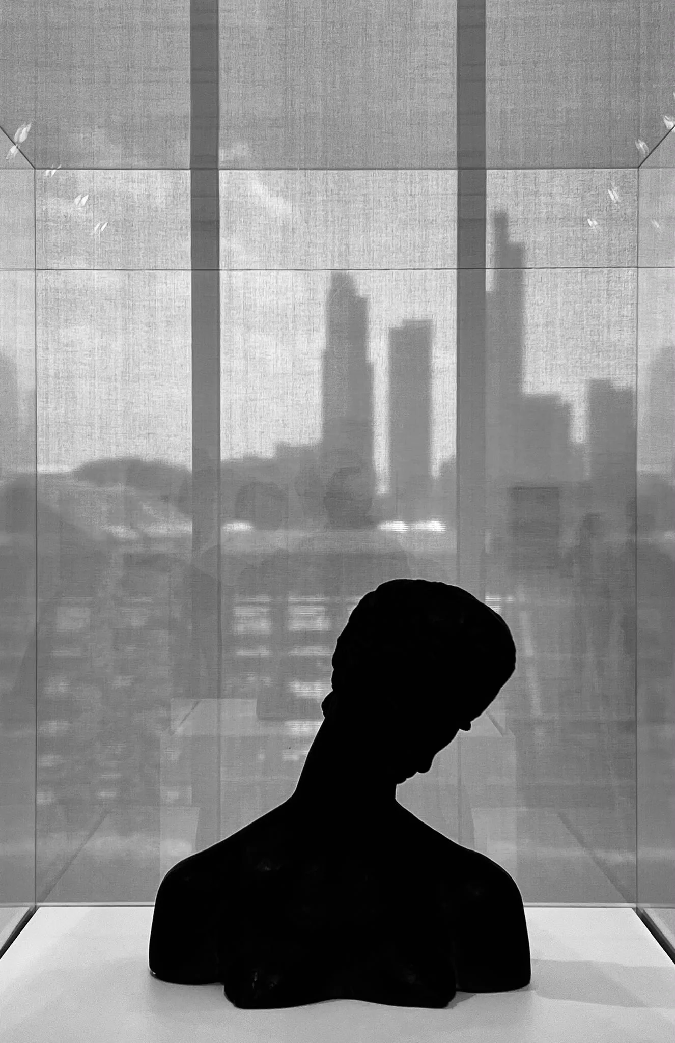 Silhouette of a person with short hair looking down, standing in front of a reflective glass wall showing city skyscraper reflections.