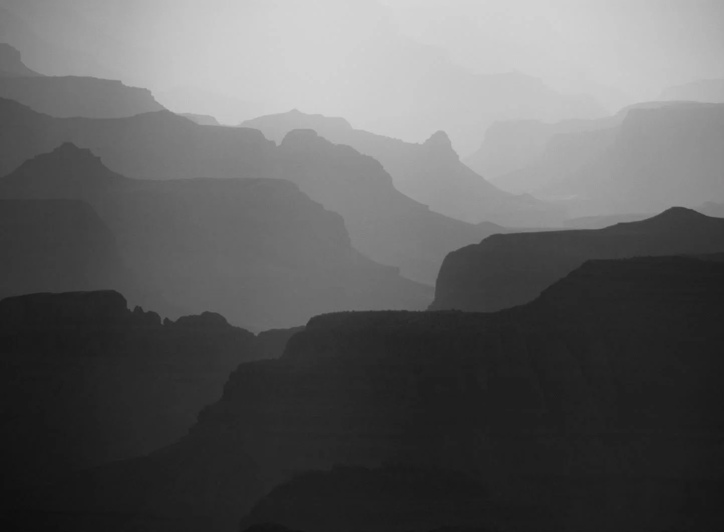Black and white photograph of layered mountain ranges fading into the distance, creating a misty and atmospheric landscape.