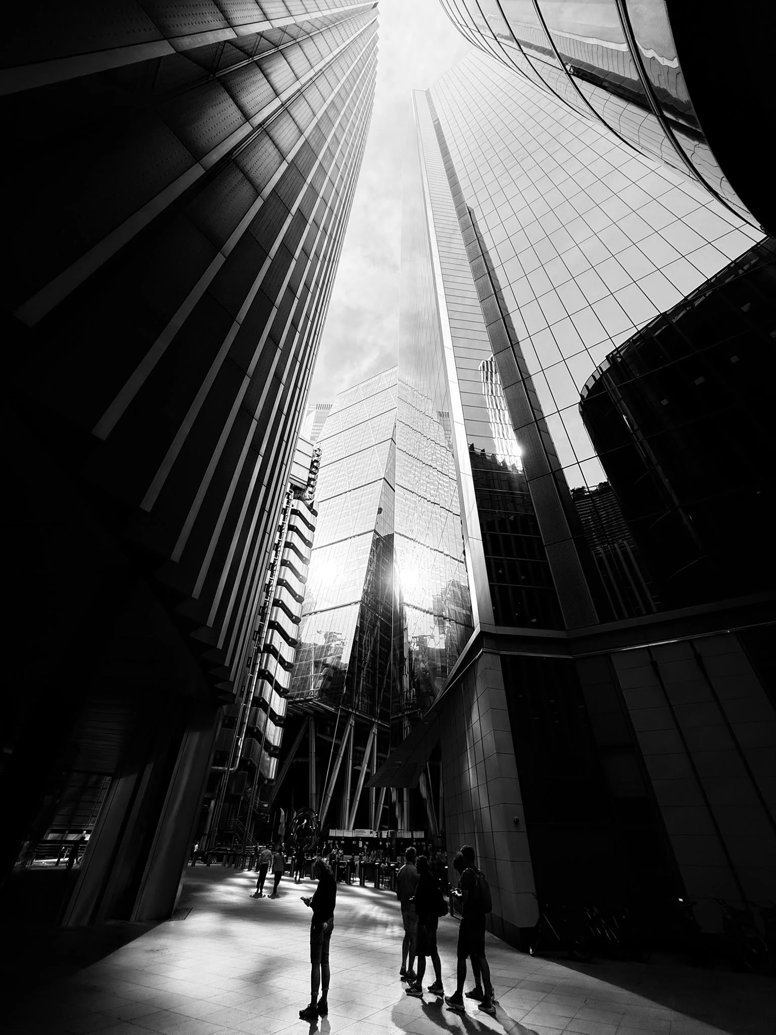 View of tall modern skyscrapers with glass facades from the street level, people walking and standing below, black and white photography.