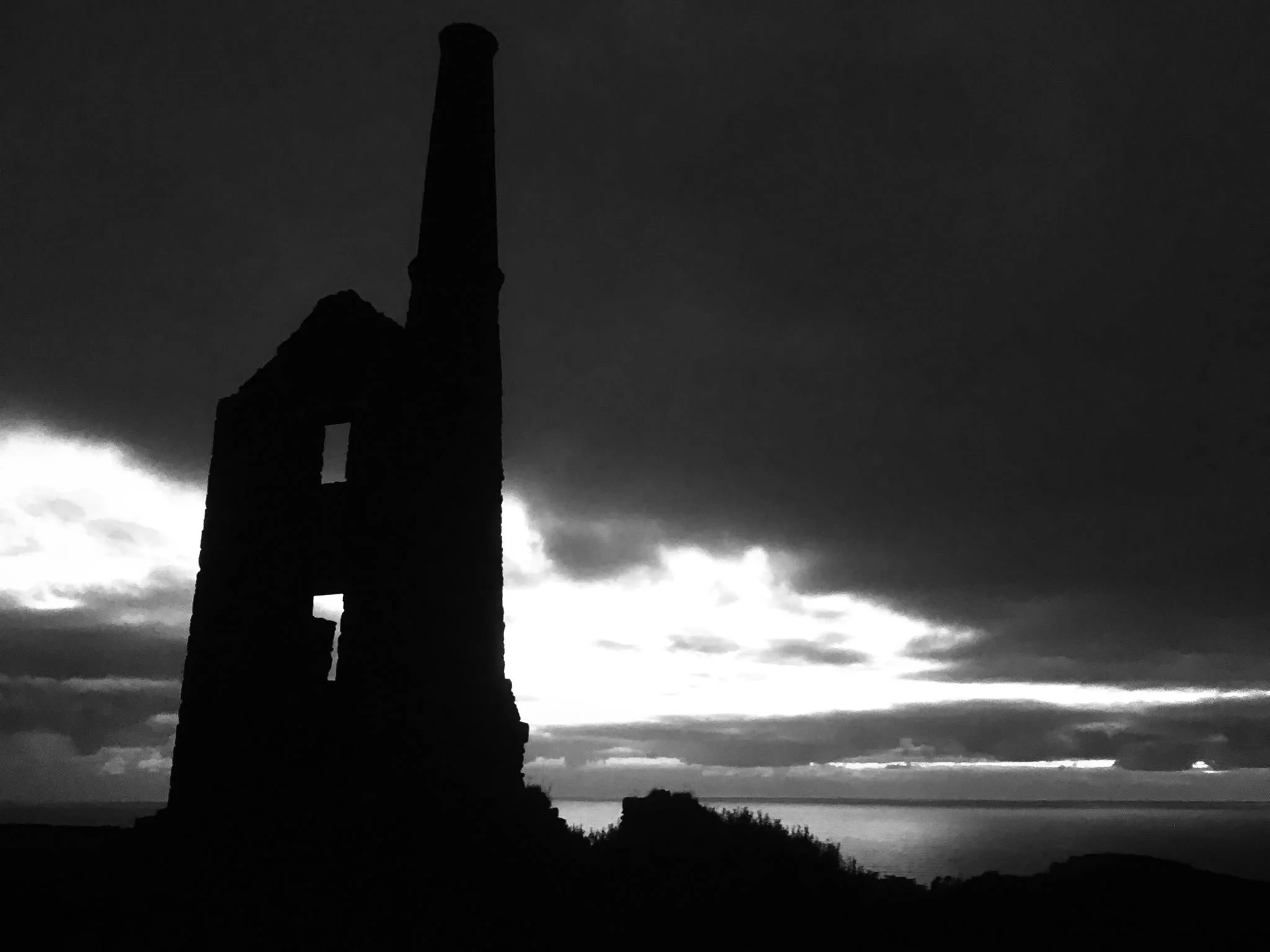 Silhouette of a tall, historic lighthouse or church steeple against a cloudy sky during dusk or dawn.