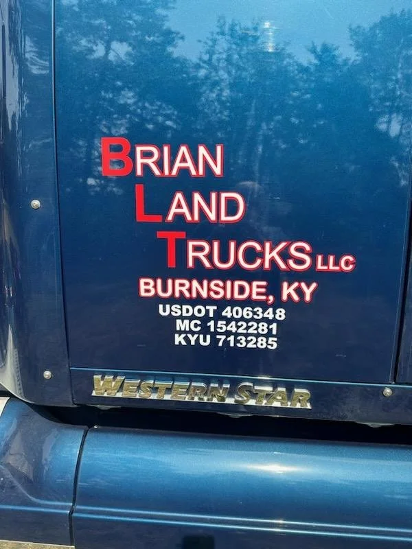 Close-up of a blue truck door with red and white text displaying business information for Brian Land Trucks LLC in Burnside, Kentucky, along with USDOT, MC, and KYU numbers, and a Western Star logo.