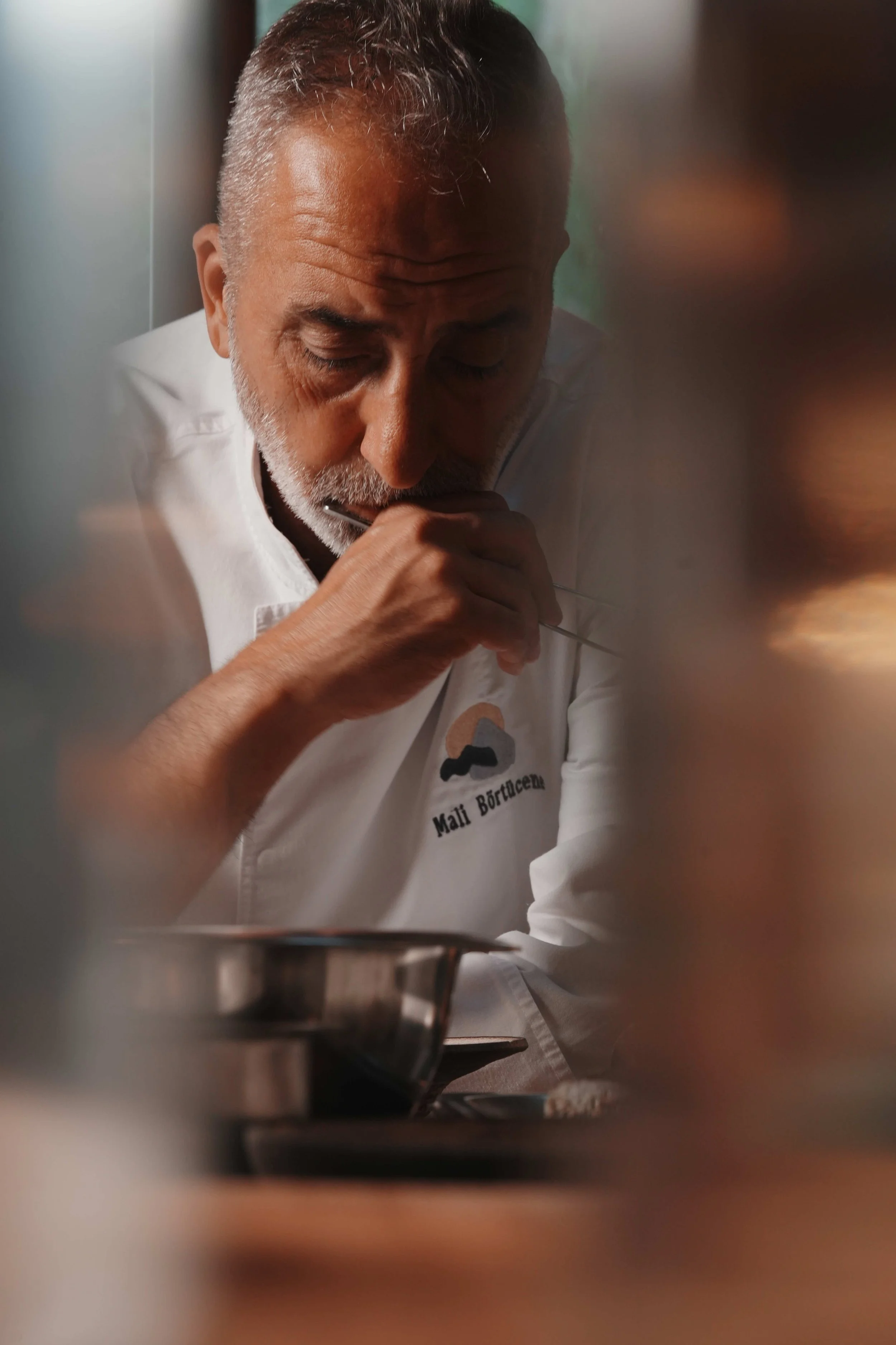 Chef Mehmet Al Börtücene is pondering or tasting food in a professional kitchen setting.