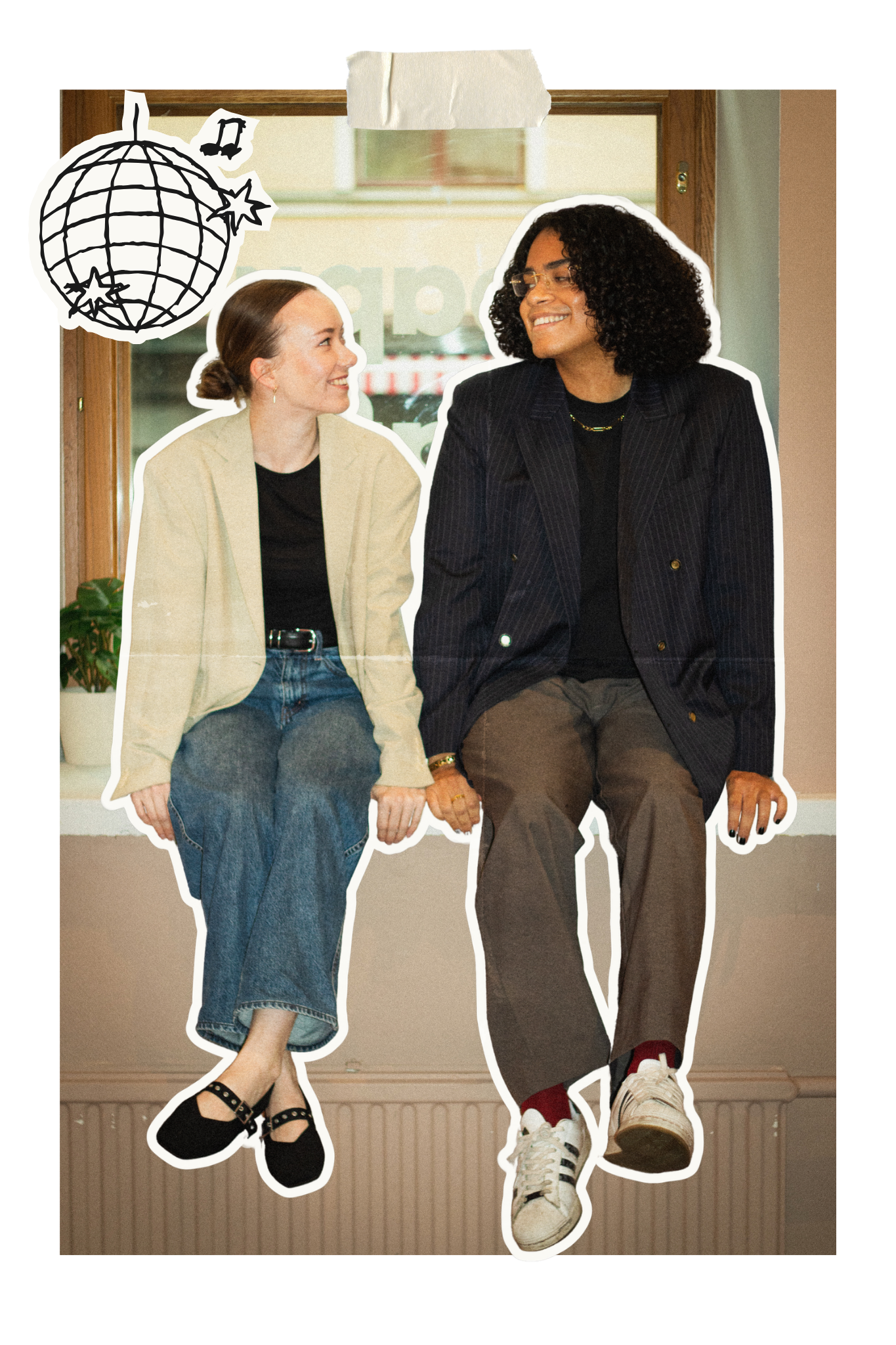 Two people sitting side by side, smiling and looking at each other, with casual clothing and sneakers. There is a drawing of a globe with stars hanging near the top left corner.