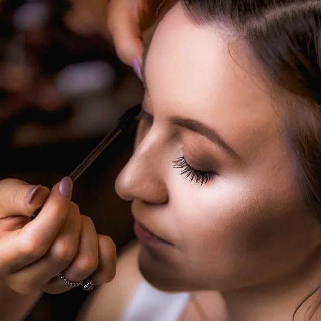 Close-up of a woman getting her makeup done, with a makeup brush near her closed eyelid.