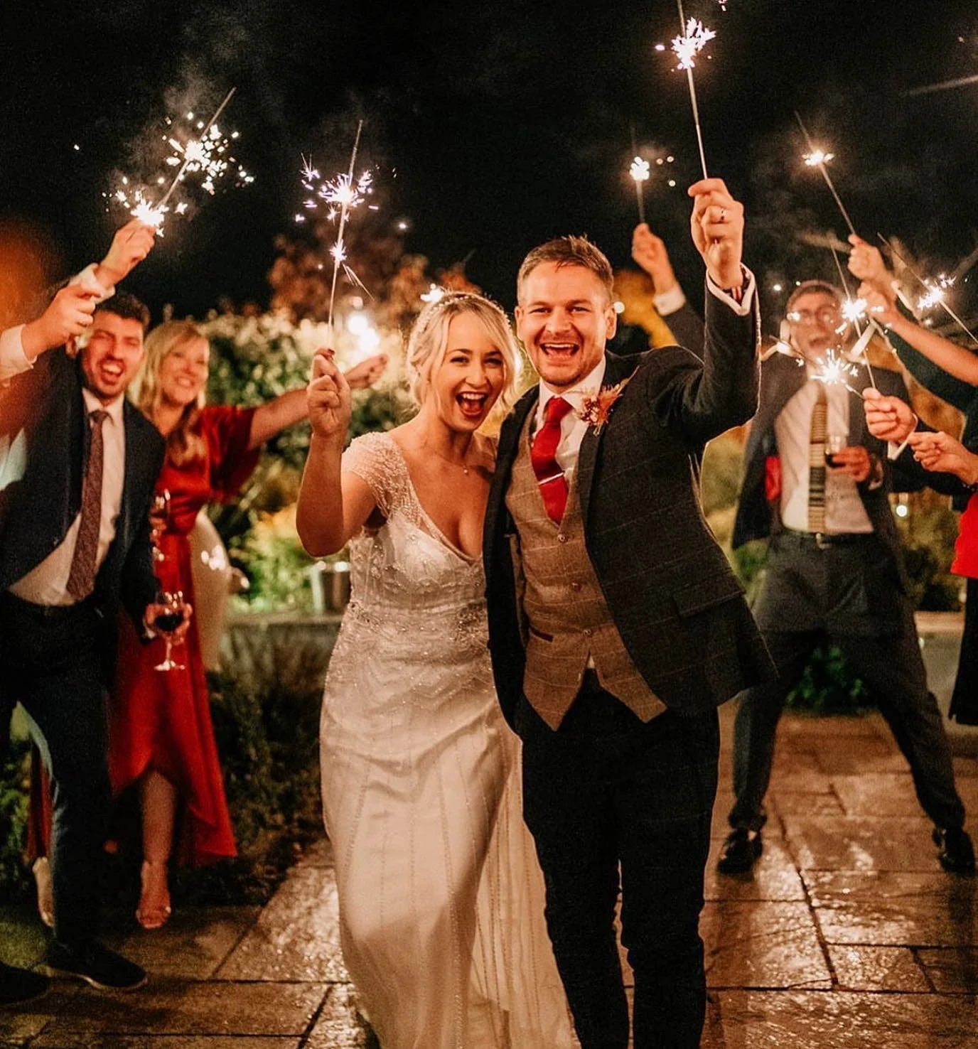 Happy newlywed couple celebrating with friends and sparklers at night.