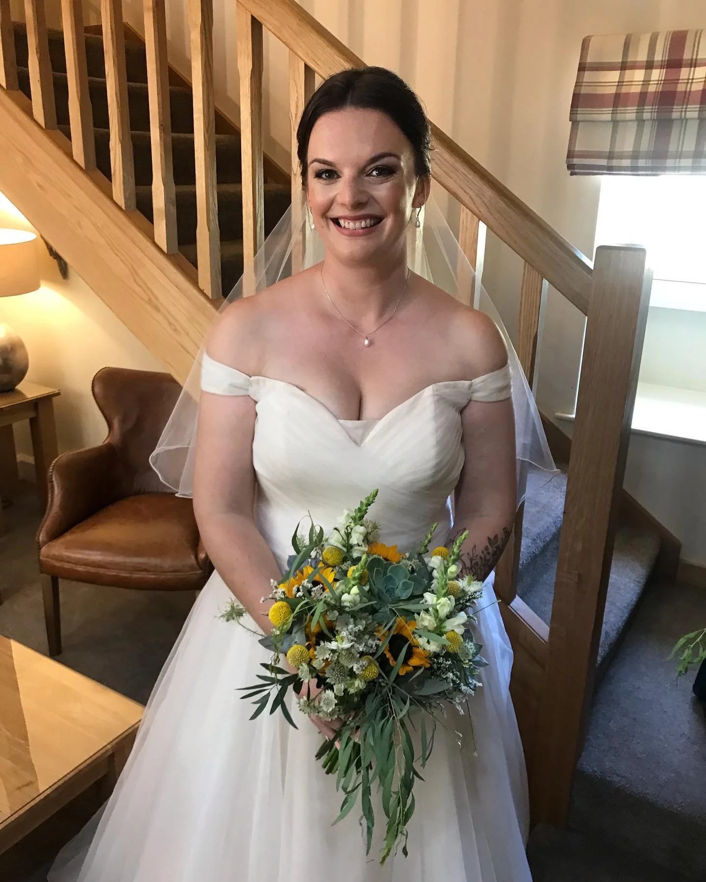 A smiling woman in a wedding dress holding a bouquet of flowers in a cozy indoor setting.