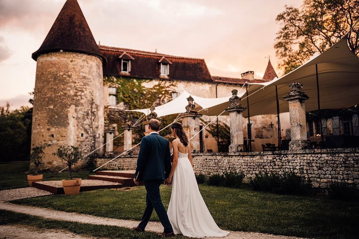 A bride and groom walking hand in hand outdoors near a historic castle.