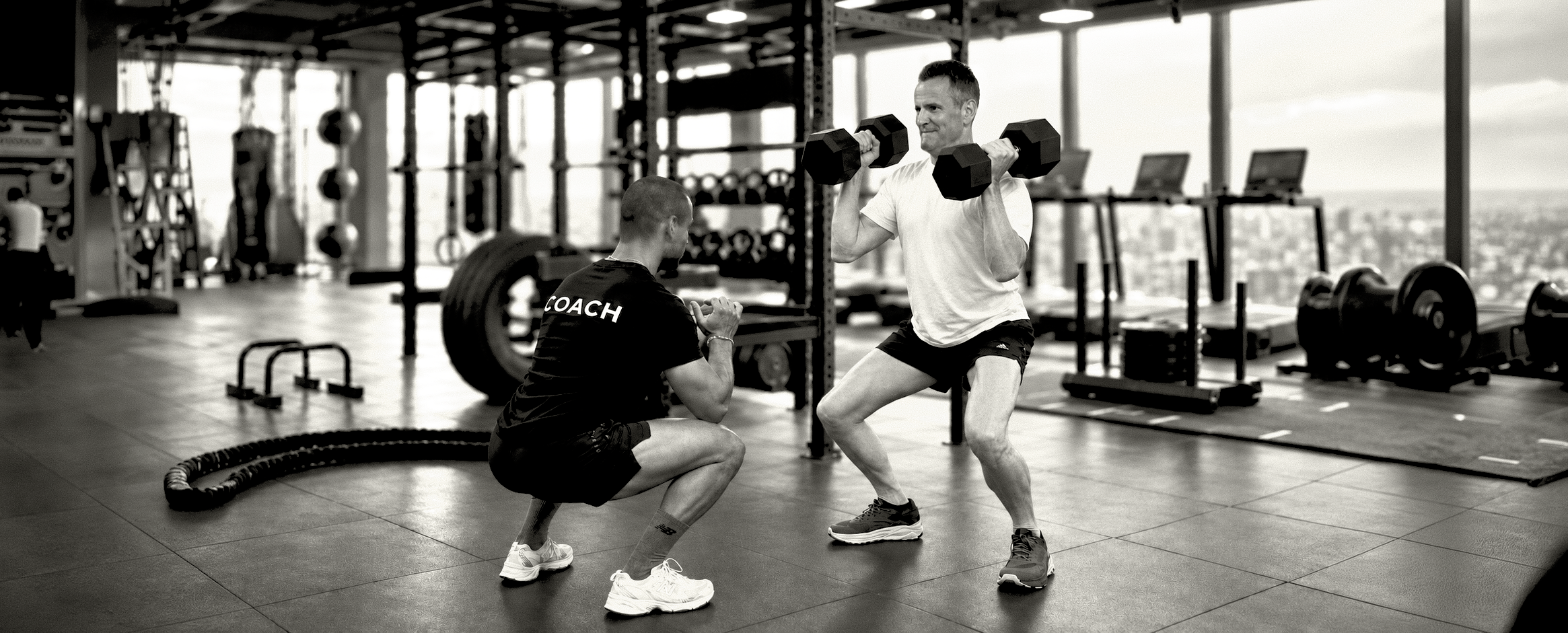 Personal trainer coaching a client through a dumbbell squat in a London gym.