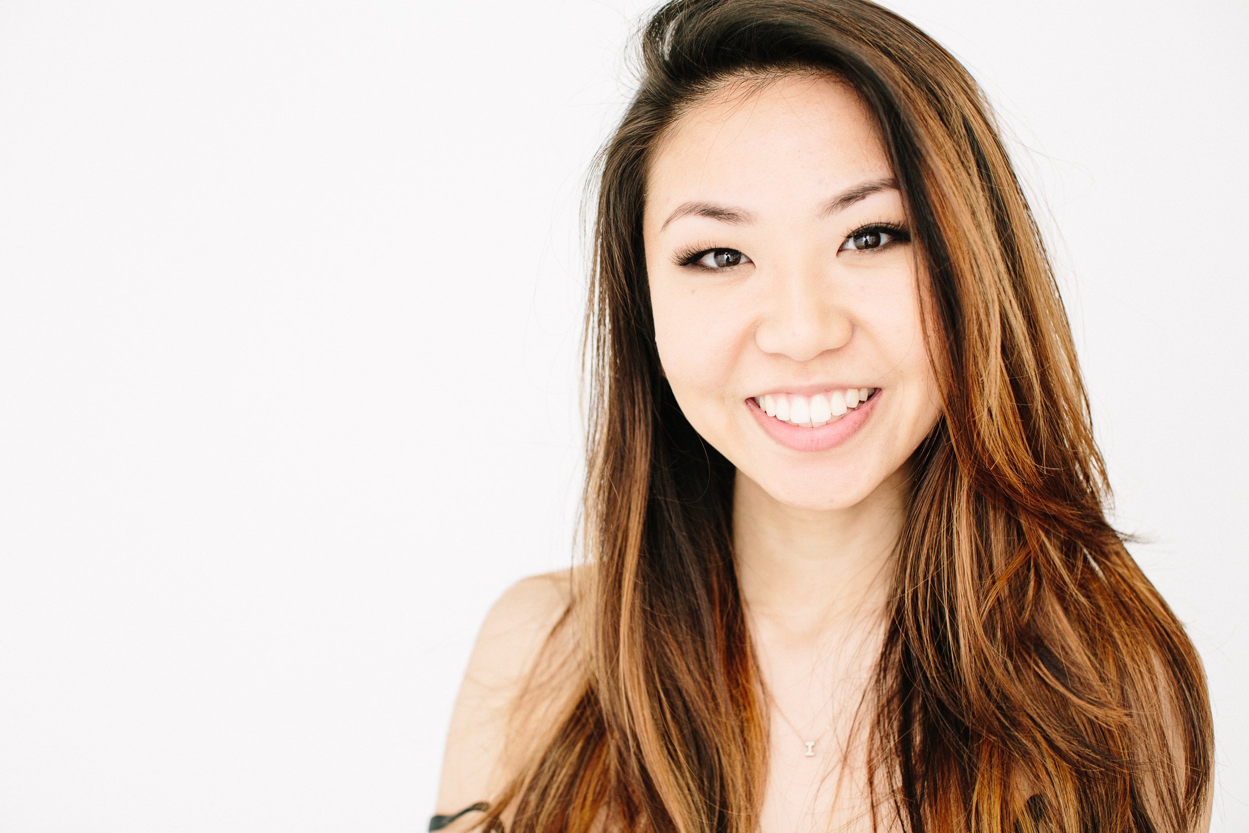 Close-up of a smiling woman with long, wavy brown hair and light skin against a white background.
