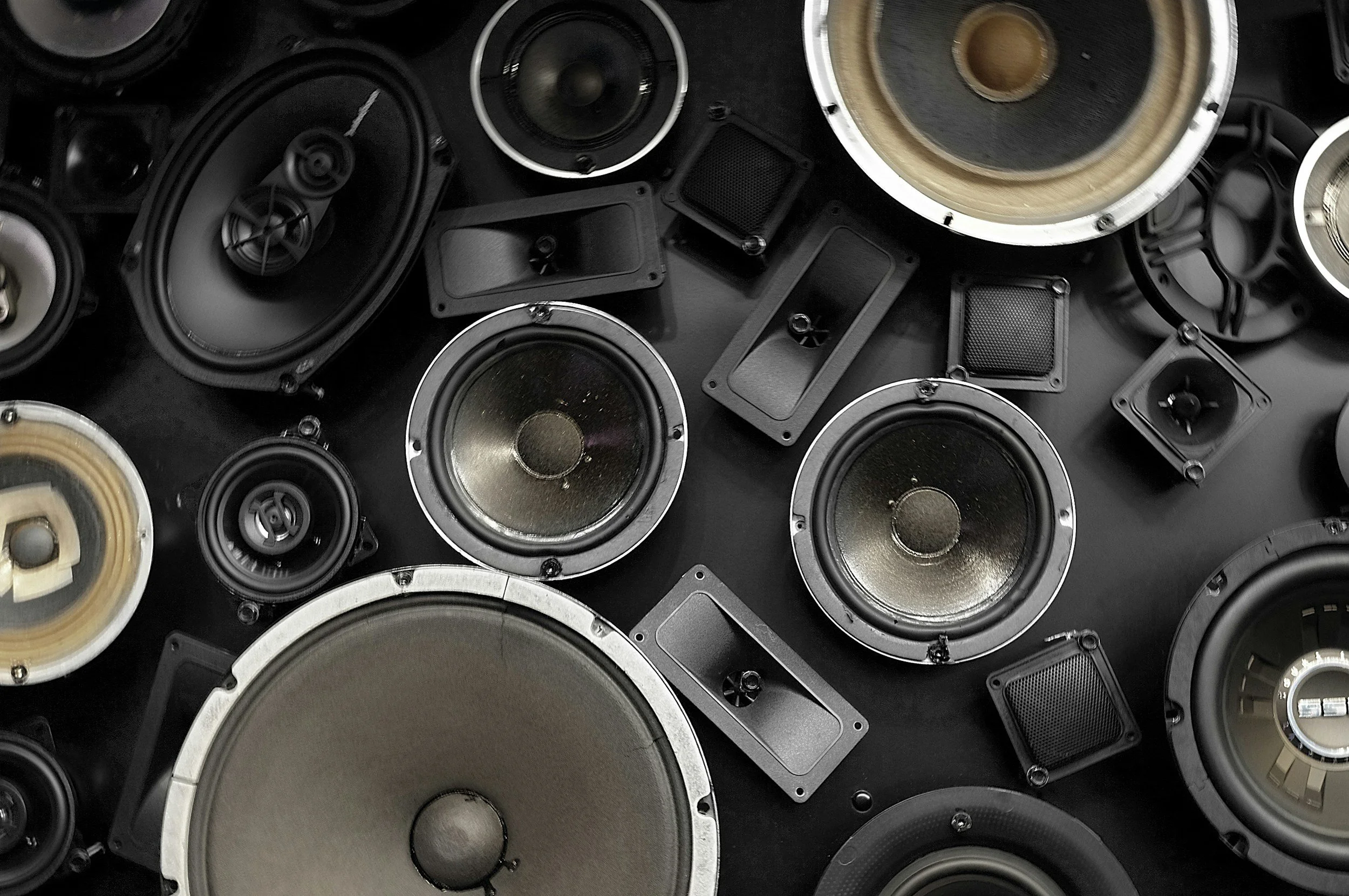 A collection of various speakers and speaker components arranged together, with some showing speaker cones and others showing clips and frames.