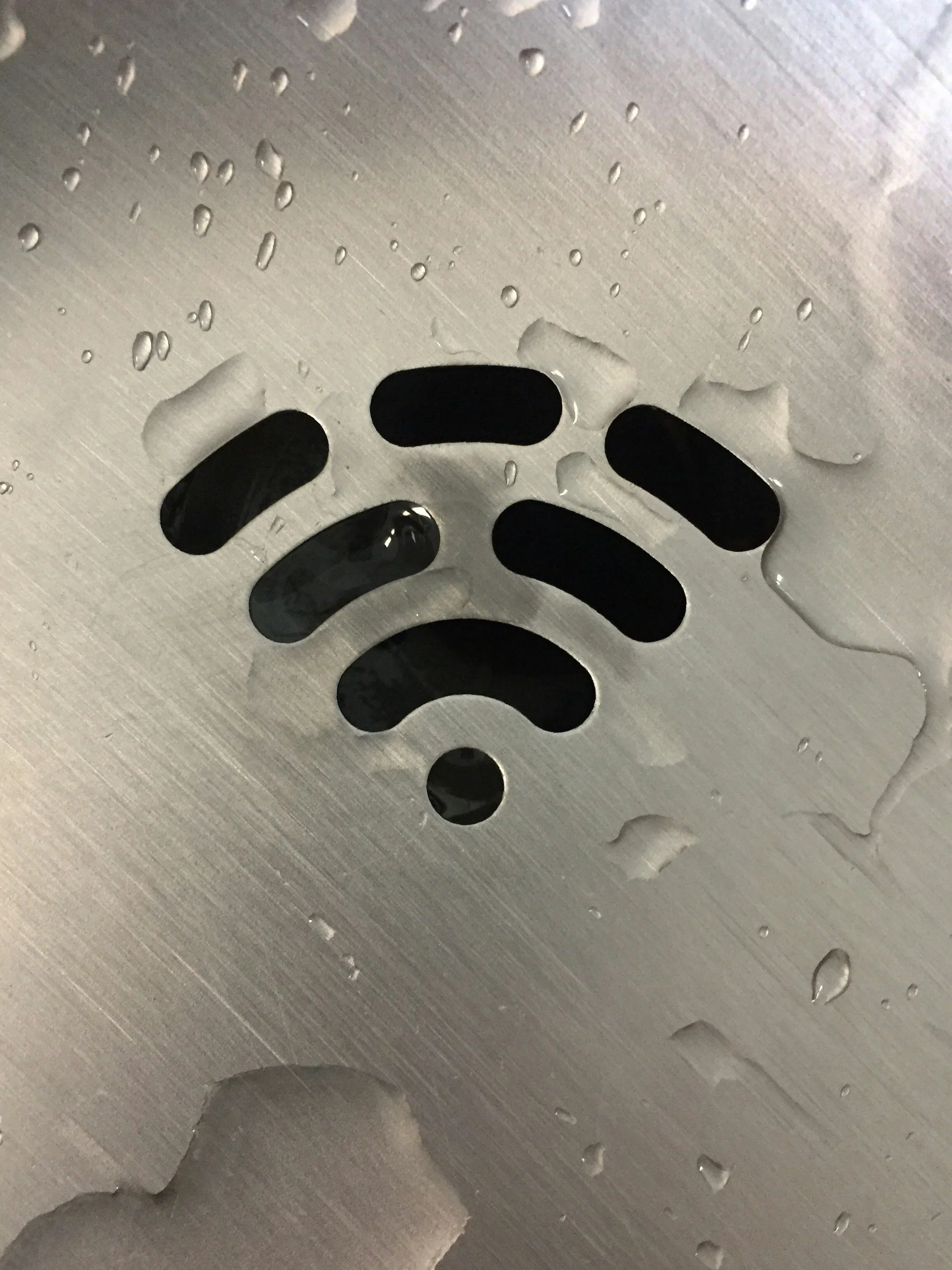 Close-up of a metallic surface with water droplets and a drainage hole.