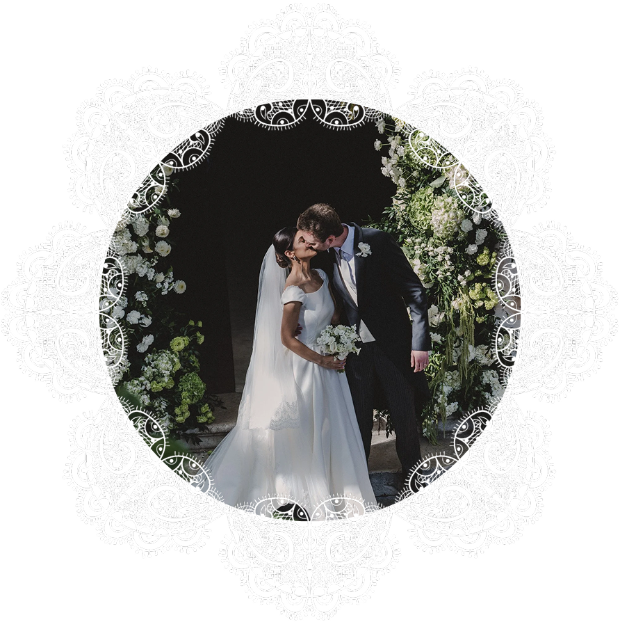 Un couple de mariés s'embrassant lors de leur mariage, entouré de décorations florales et d'un cadre en dentelle blanche sur fond noir.