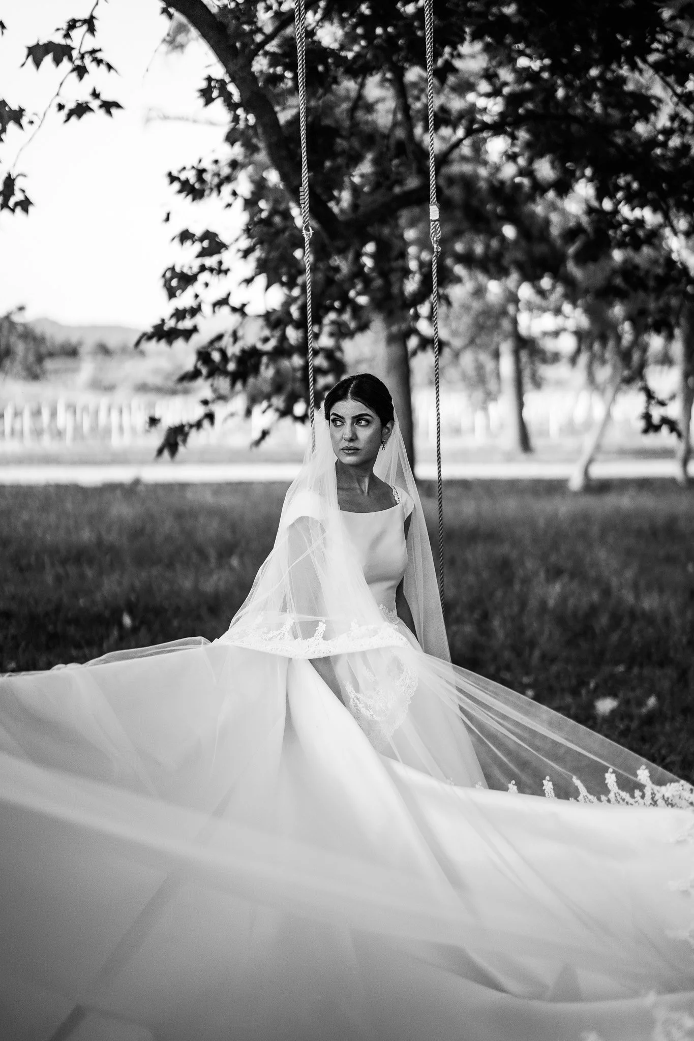 Femme en robe de mariée assise sous un arbre, vue en noir et blanc.