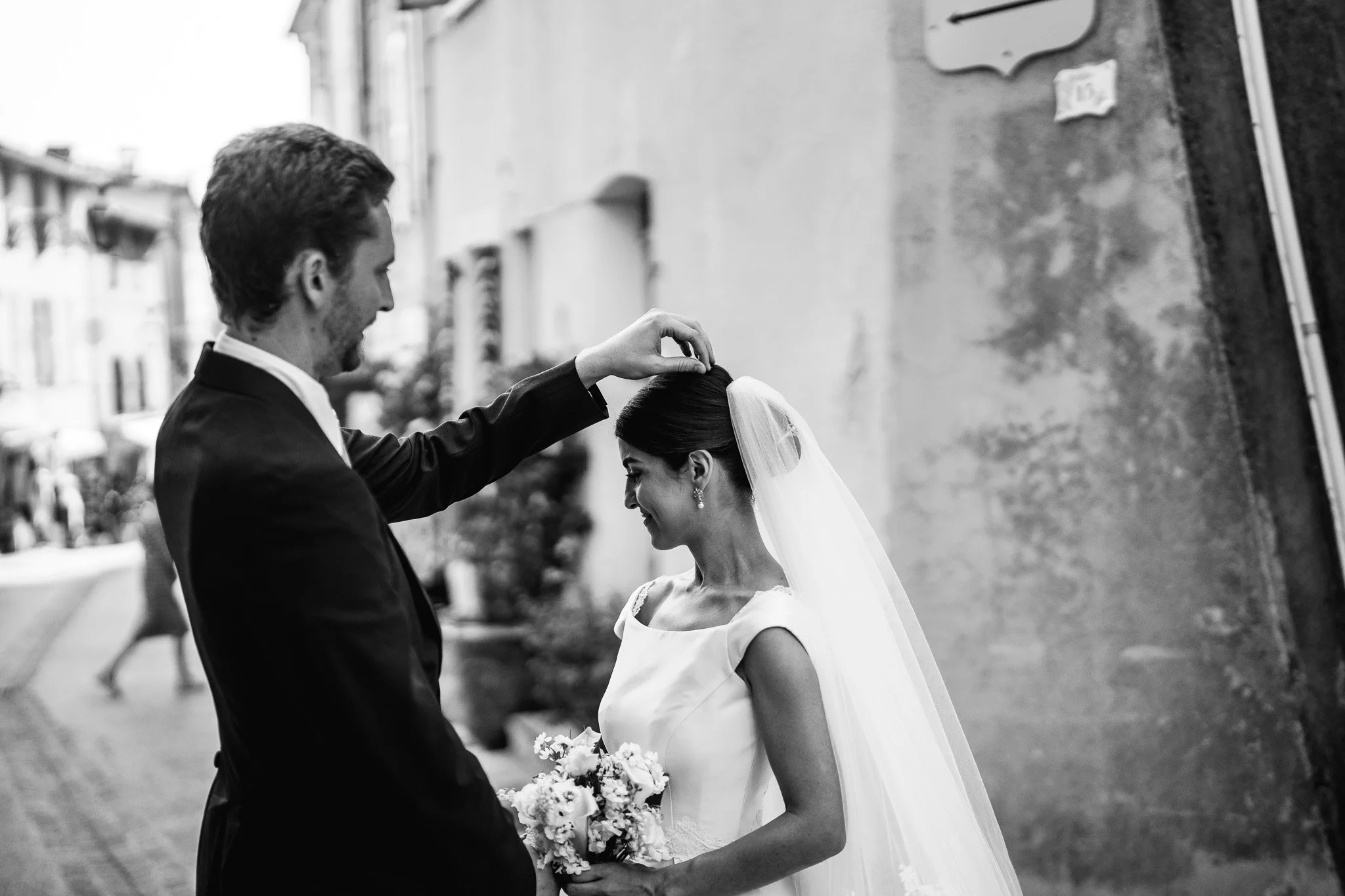 Un couple lors d'un mariage, la mariée en robe blanche avec une voile, le marié en costume noir, se tenant la main devant un mur en pierre.