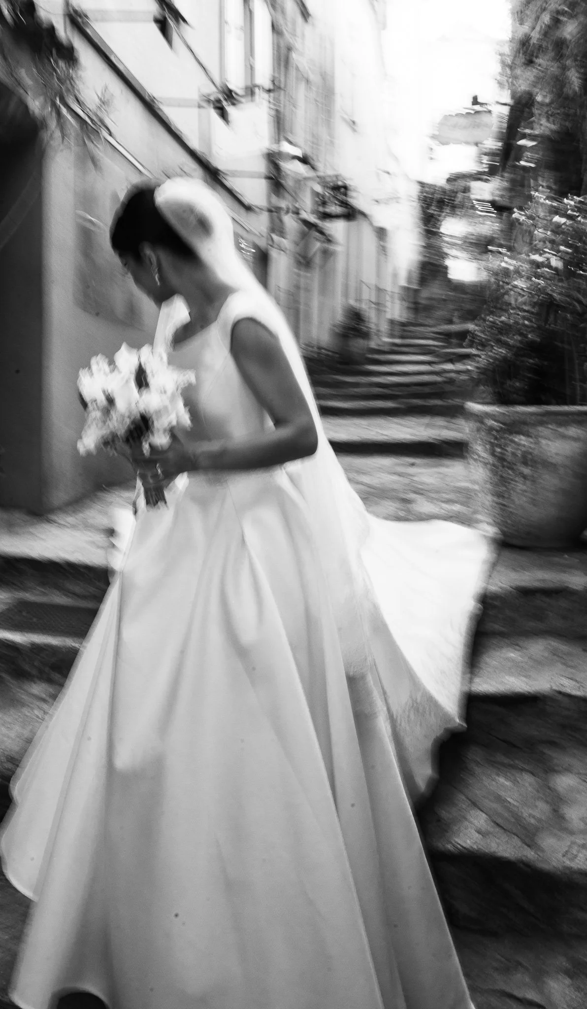 Femme portant une robe blanche, tenant un bouquet de fleurs, en marchant dans une rue pavée.